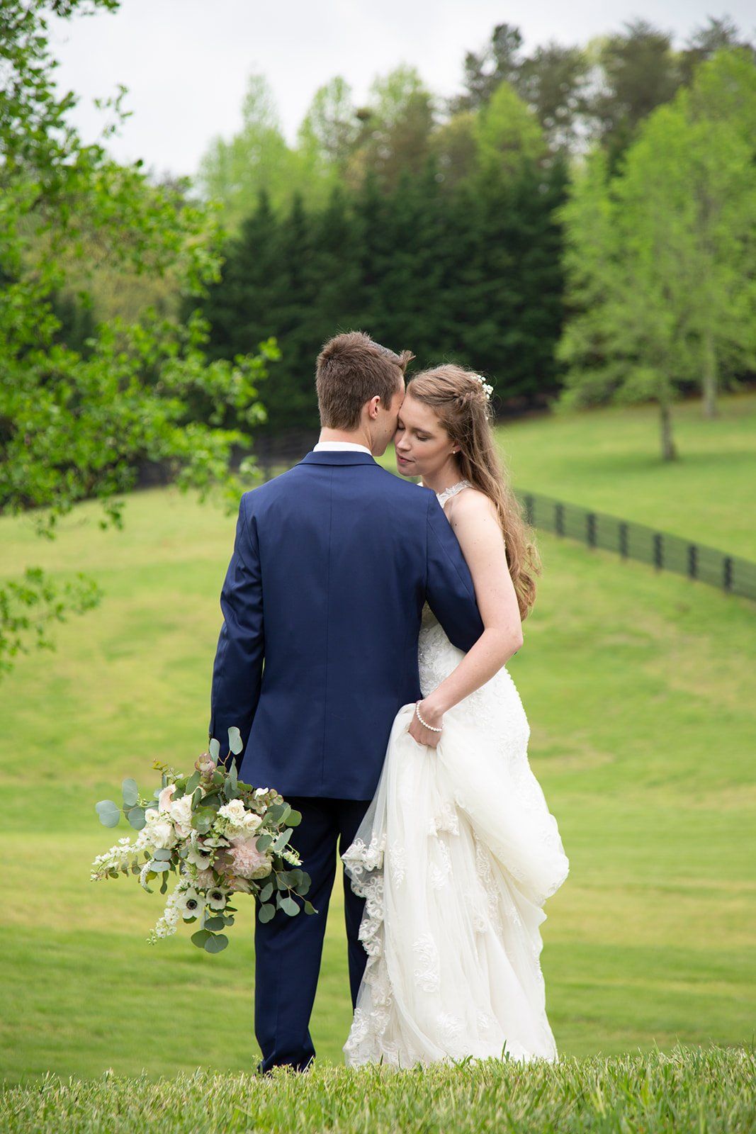 A bride and groom are kissing in a field. the bride is holding a bouquet of flowers.