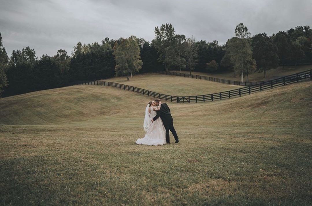 A bride and groom are kissing in a grassy field.