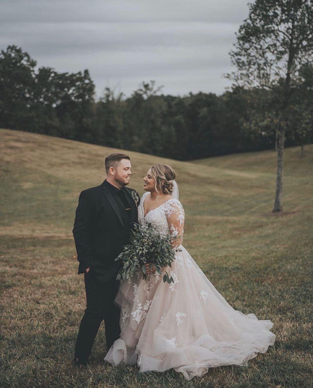 A bride and groom are standing in a field looking at each other.