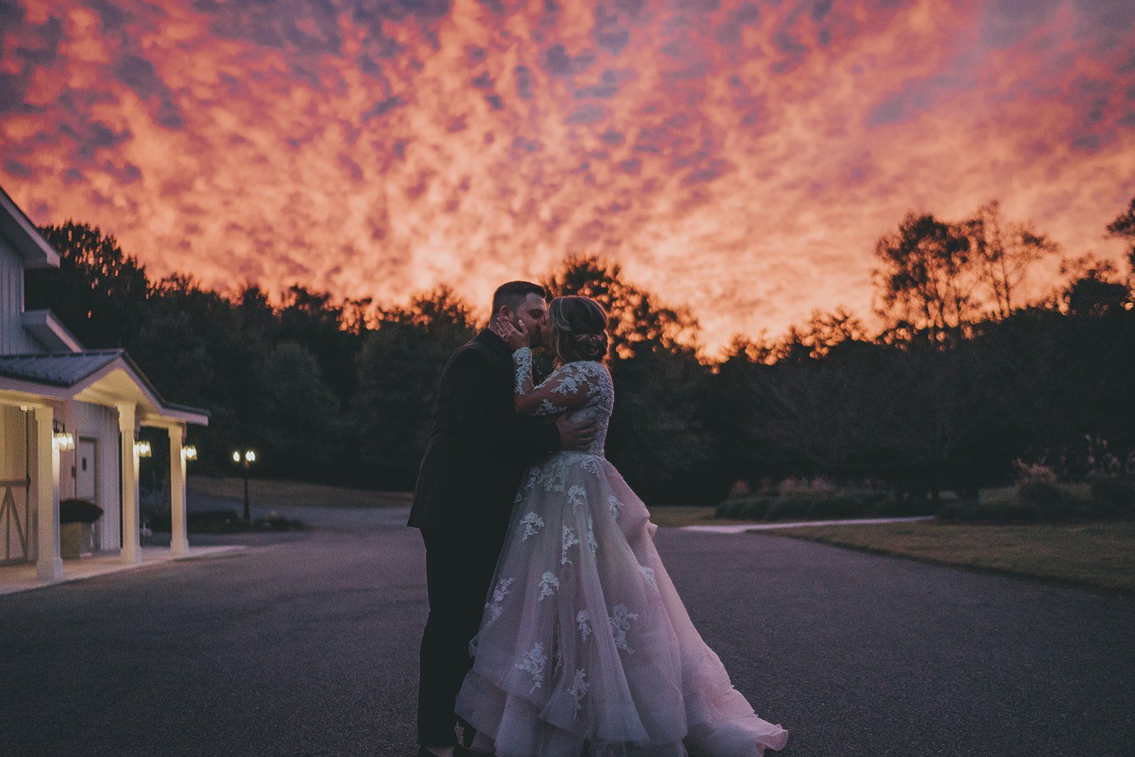 A bride and groom are kissing in front of a sunset.