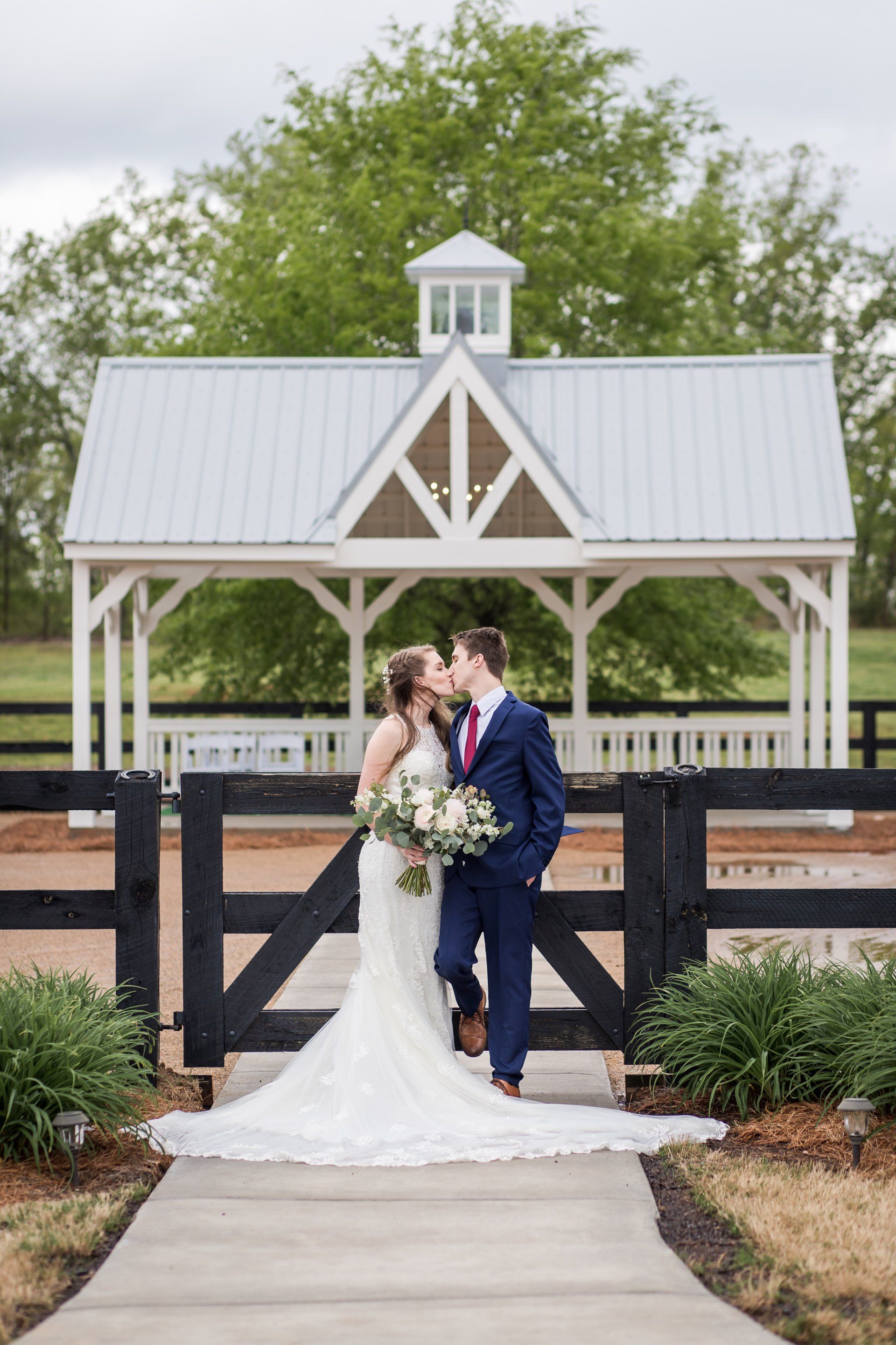 A bride and groom are kissing in front of a gazebo.