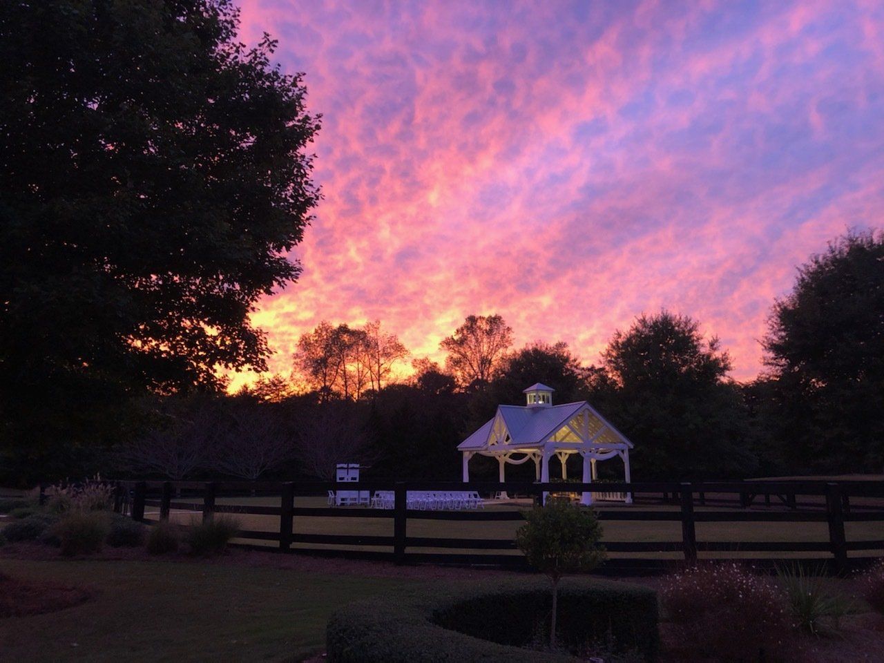 A sunset with a gazebo in the foreground and a fence in the background