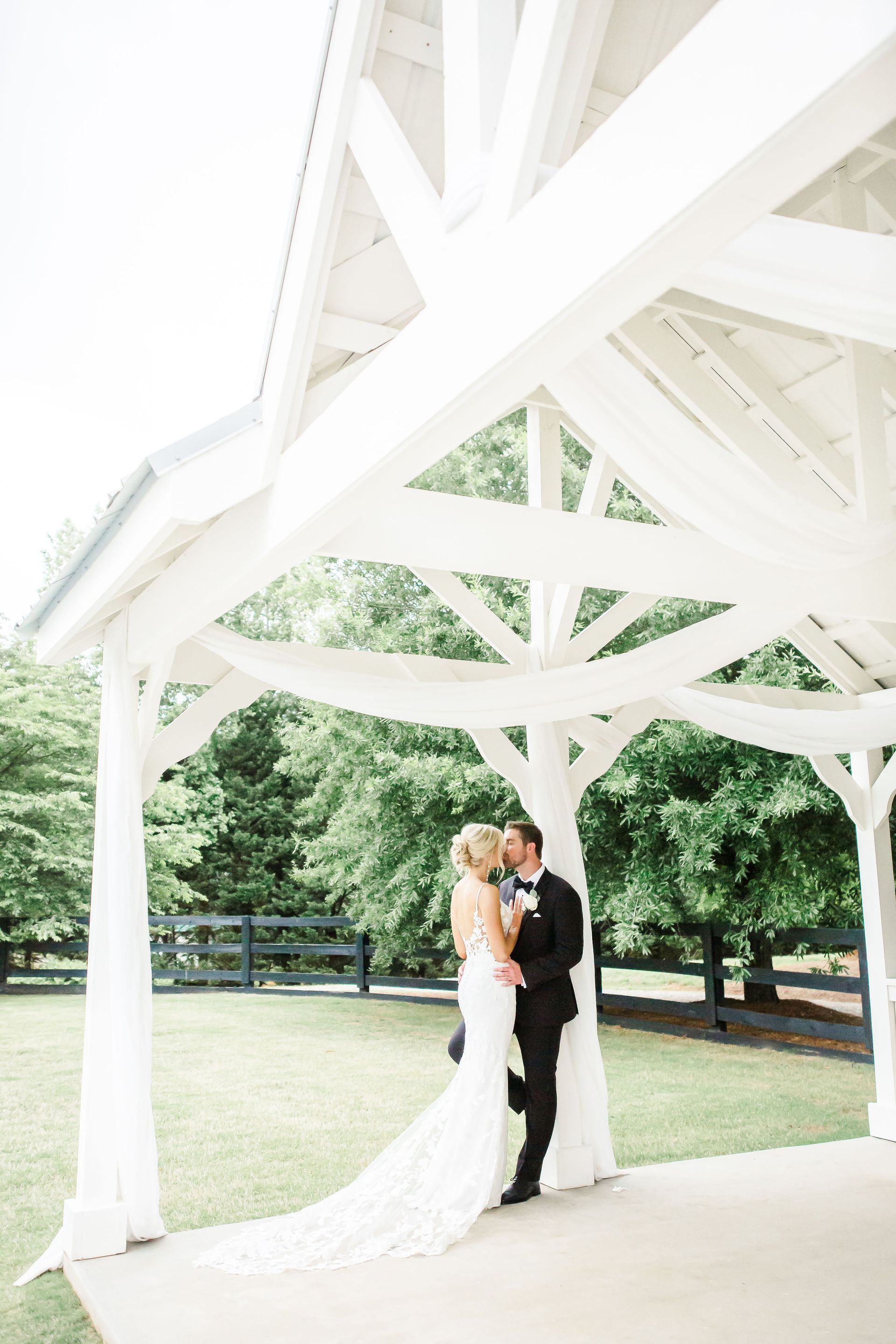 A bride and groom are kissing under a white gazebo.