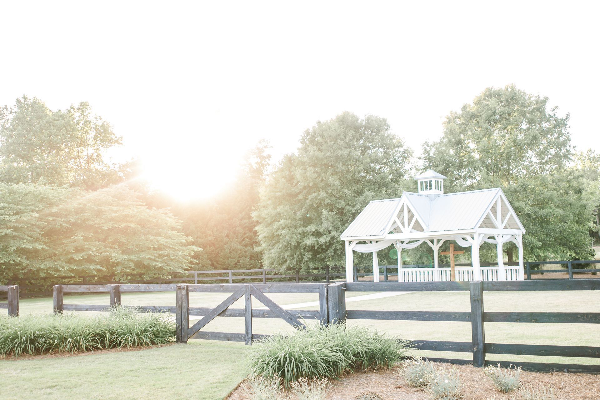 A white gazebo is behind a black fence in a field.