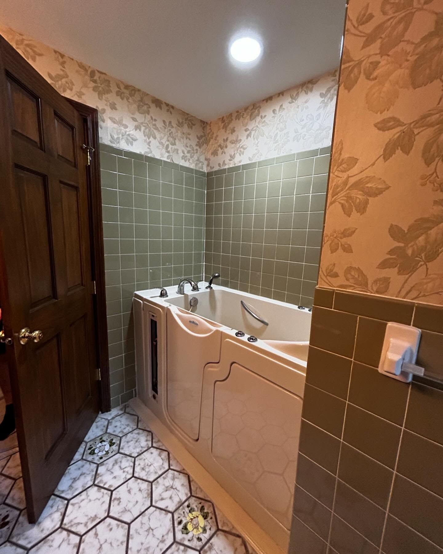 Bathroom with walk-in tub, tiled walls, floral wallpaper, and a patterned floor.