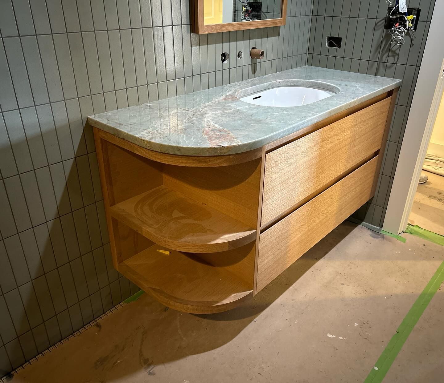 Light wood floating bathroom vanity with granite countertop, curved open shelves, and two drawers.