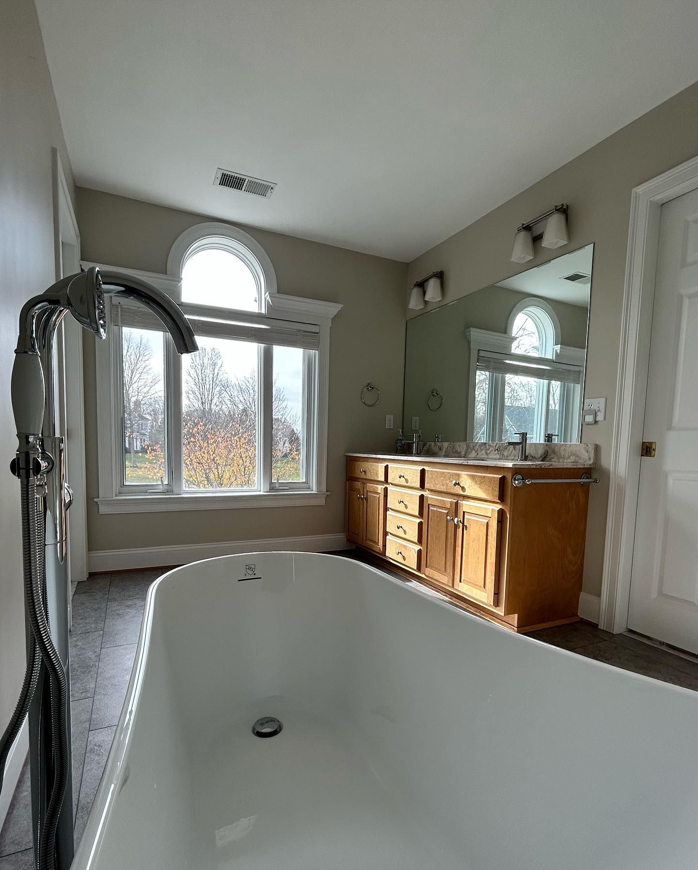 Bathroom with freestanding tub, vanity with mirror, arched window.