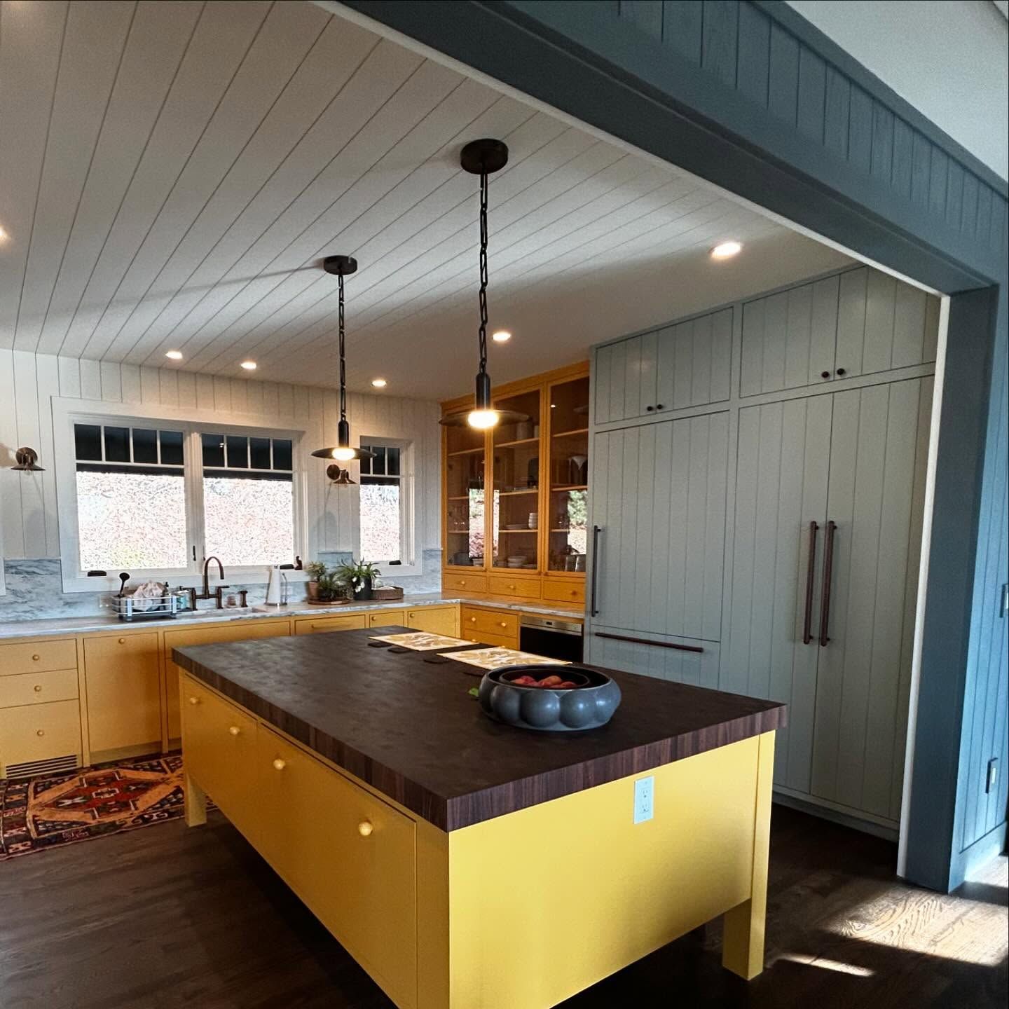 Yellow kitchen with a wooden countertop island, built-in refrigerator, and pendant lights.