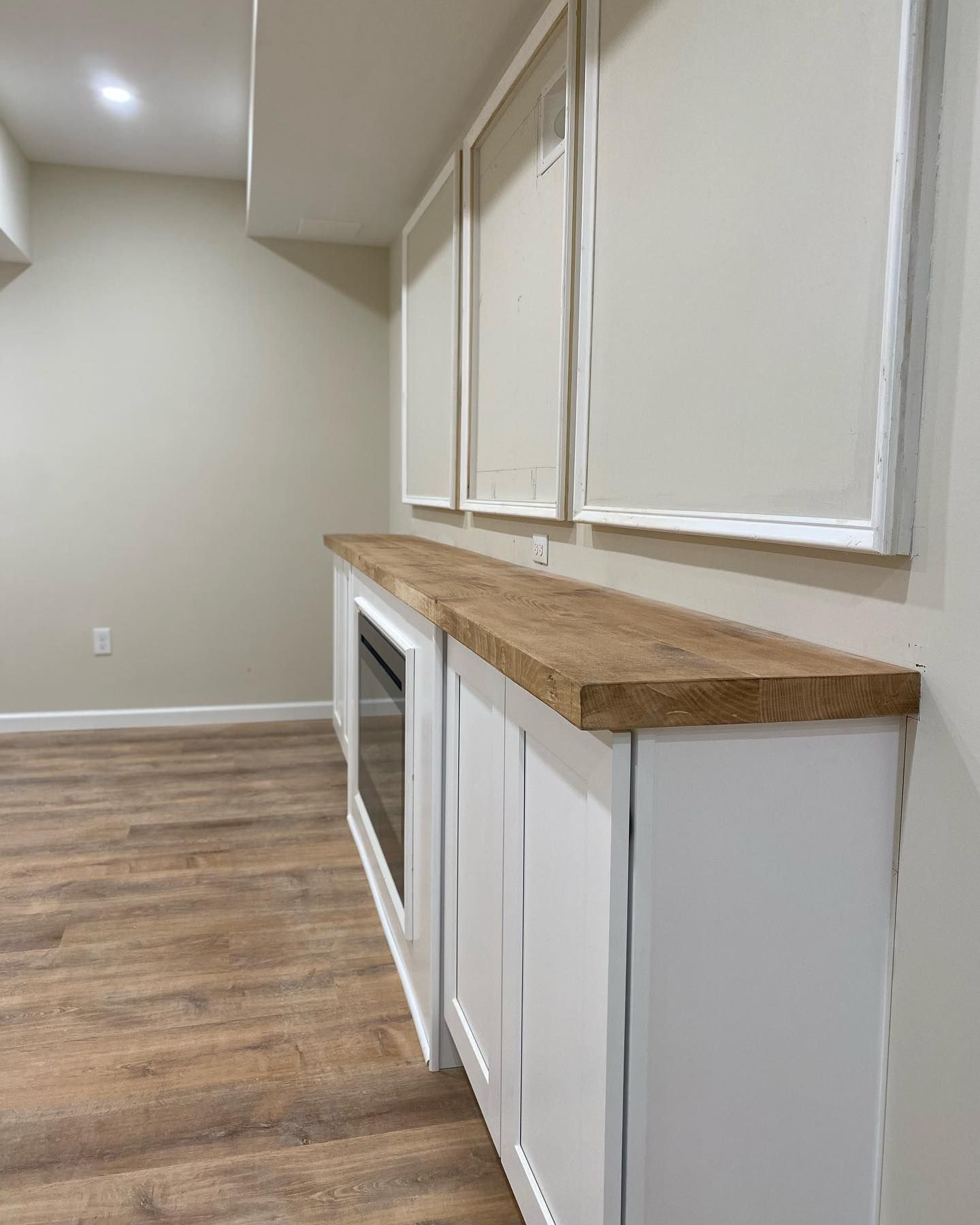 White cabinets with a wood countertop, inset fireplace, beige walls, and three decorative wall panels.