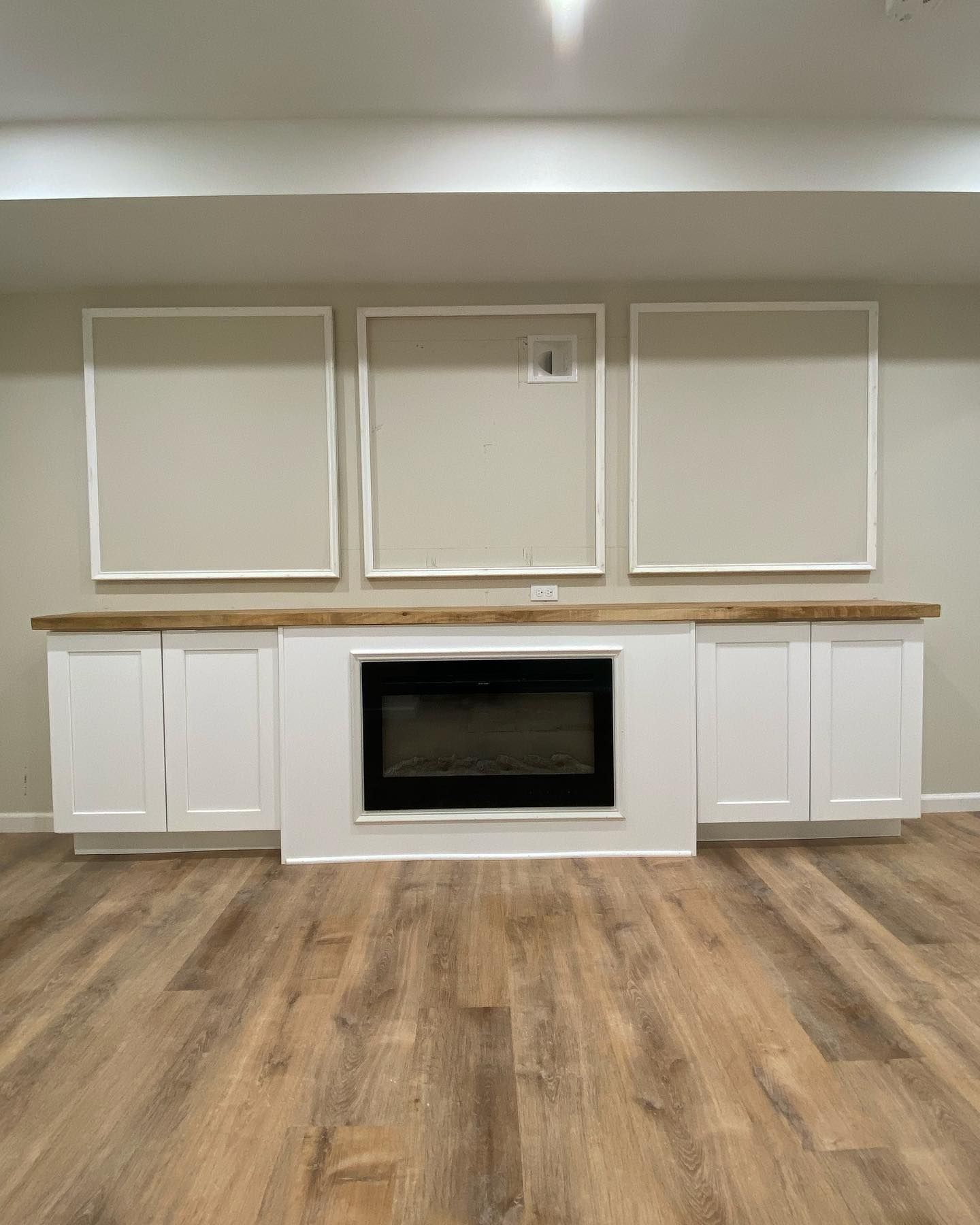 Fireplace flanked by white cabinets and three gray framed rectangles on a beige wall.
