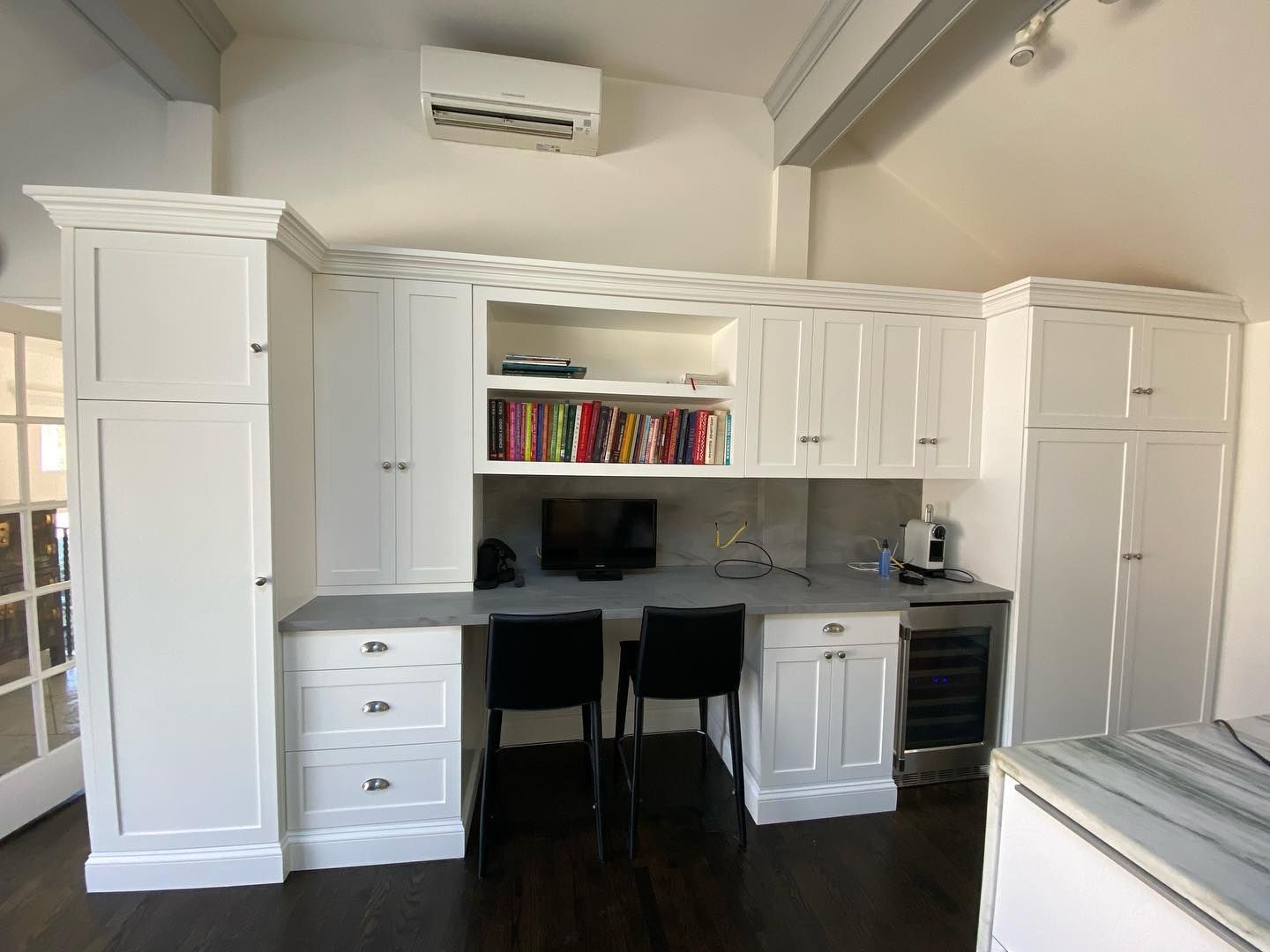 White built-in desk and cabinets with a dark countertop and black chairs in a home office.