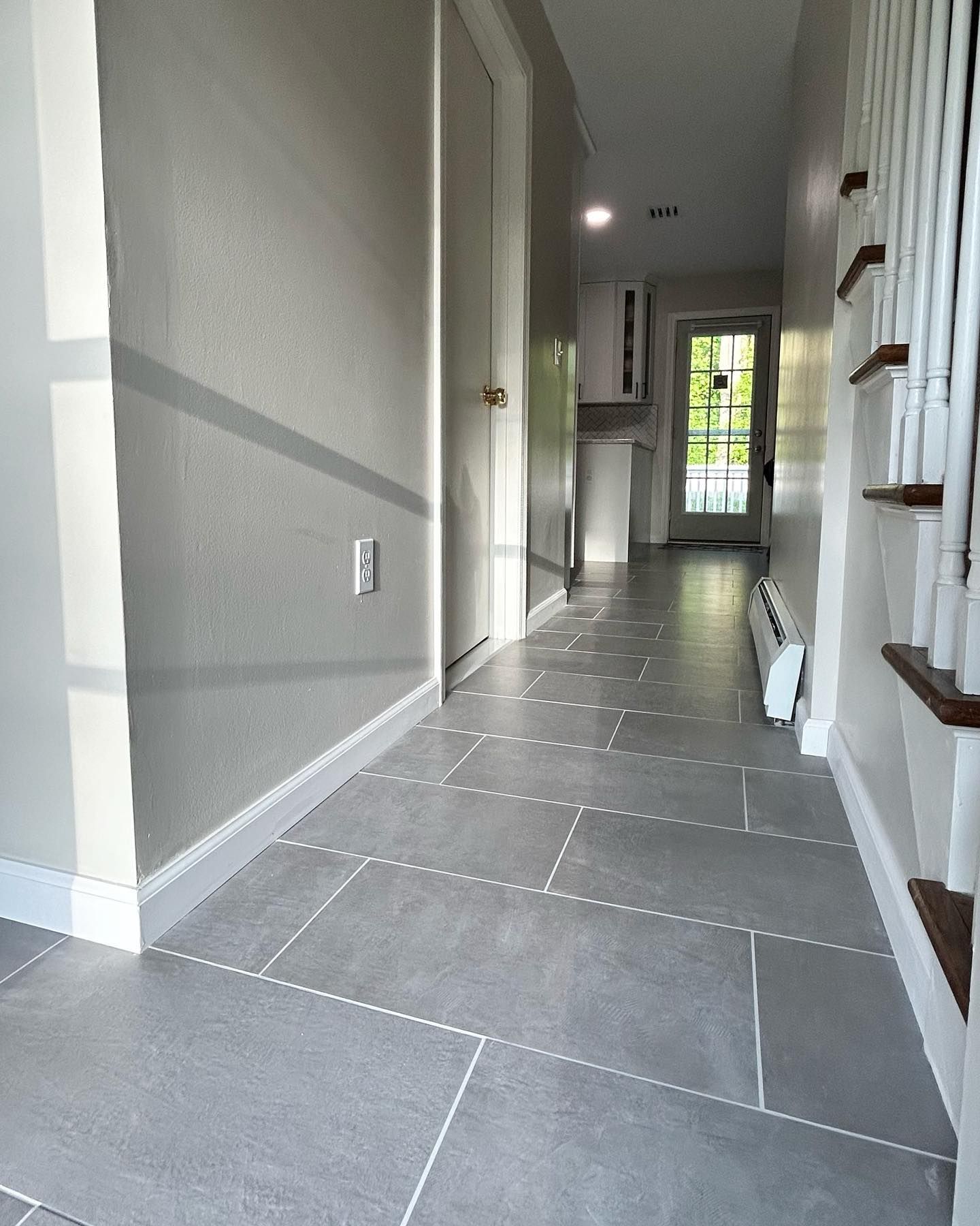 Gray tiled hallway with a door, stairs, and white trim.
