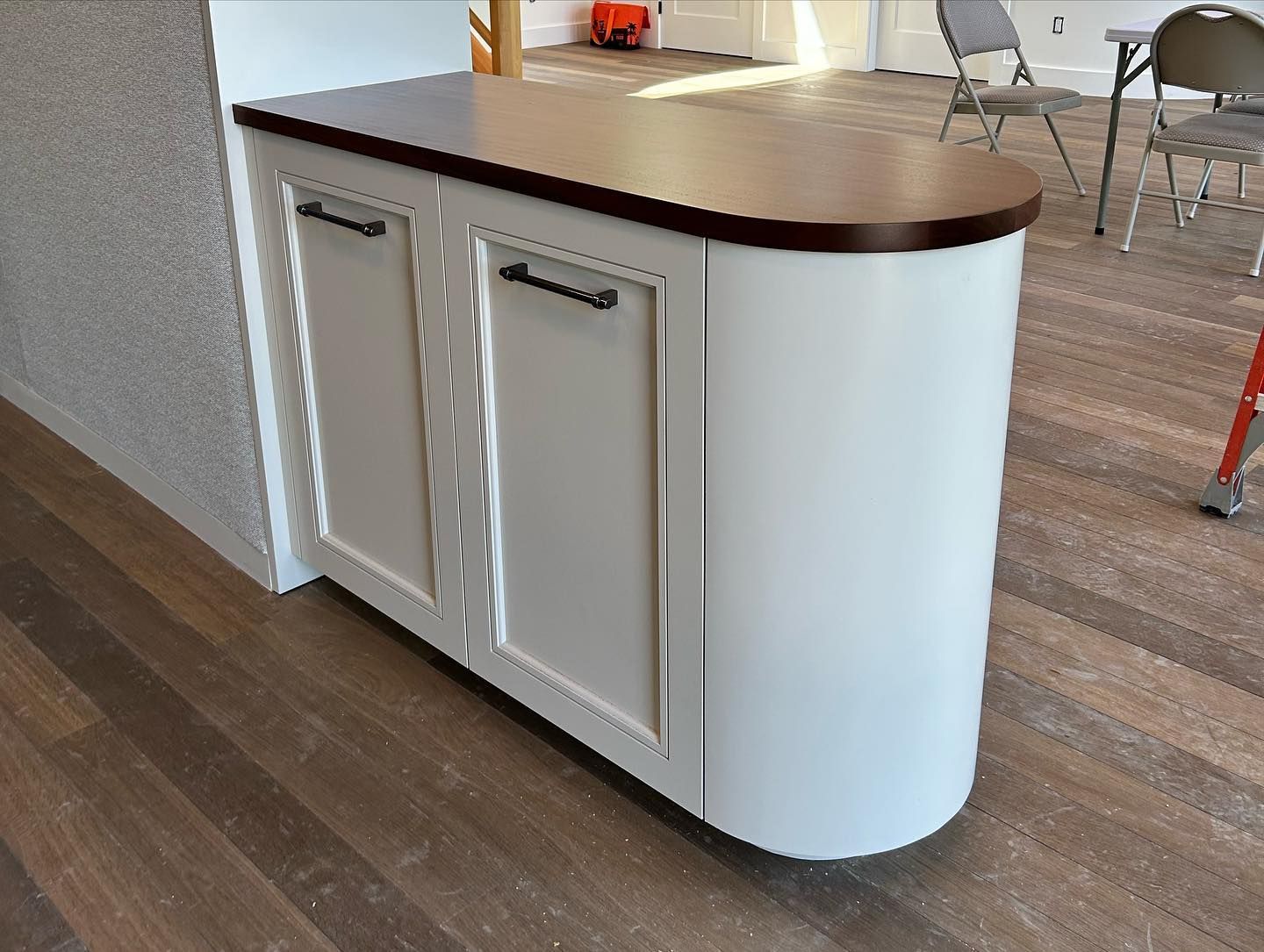 White cabinet with curved side, brown countertop, black handles, and dark wood flooring.