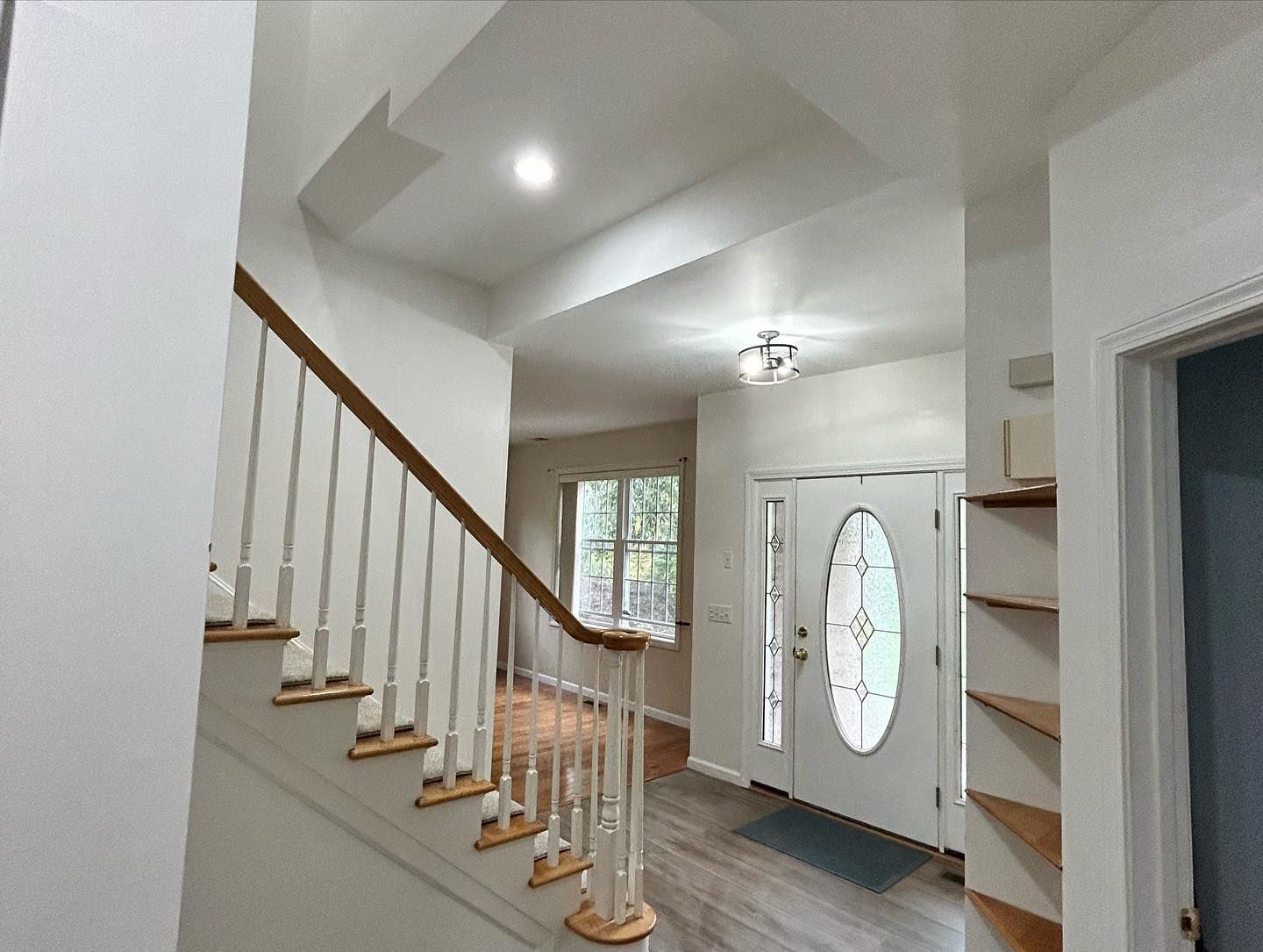 Entryway with staircase, front door, and built-in shelving. White walls, wooden stairs, and a grey doormat.