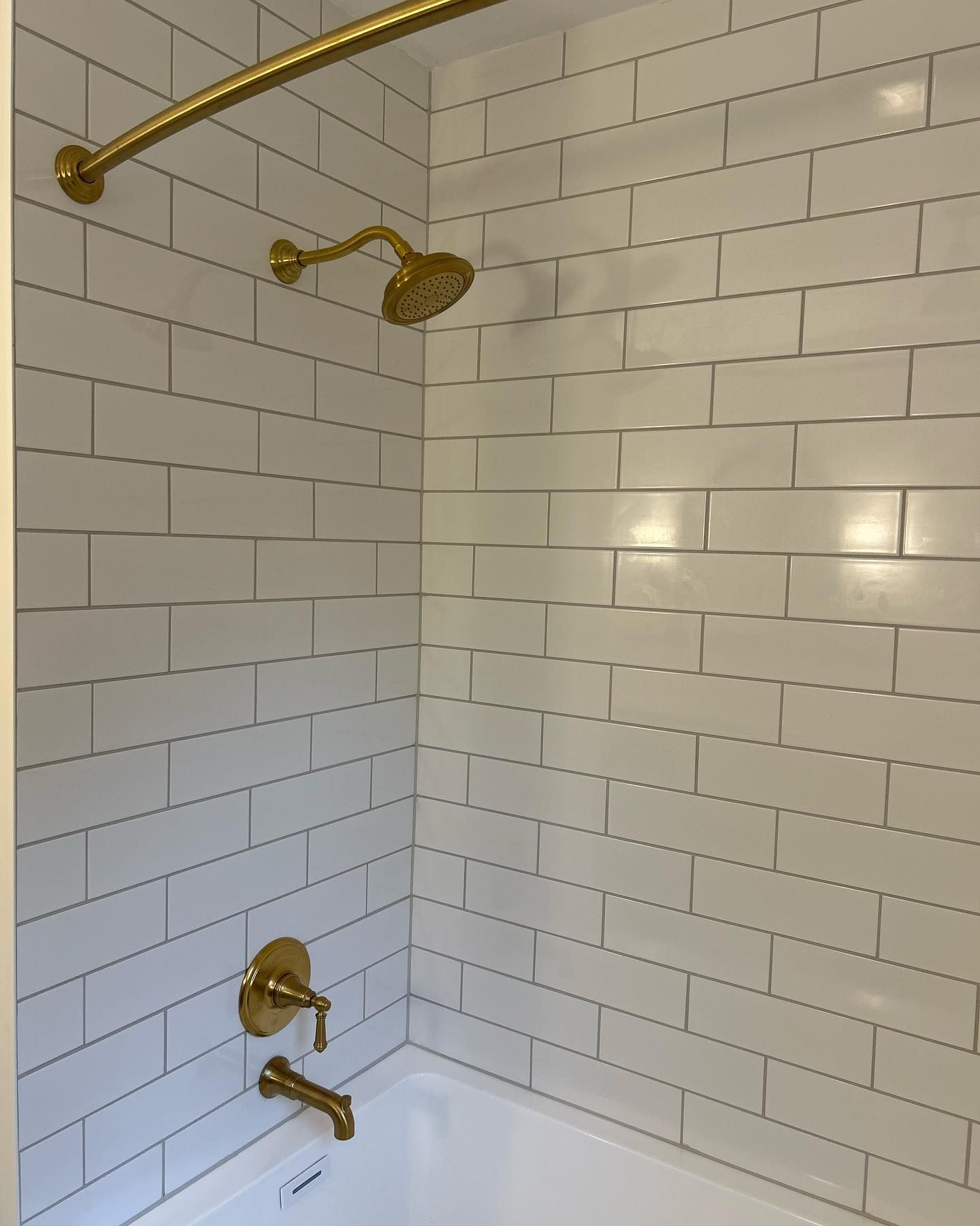 White tiled shower with gold fixtures; showerhead, faucet, curved shower rod.