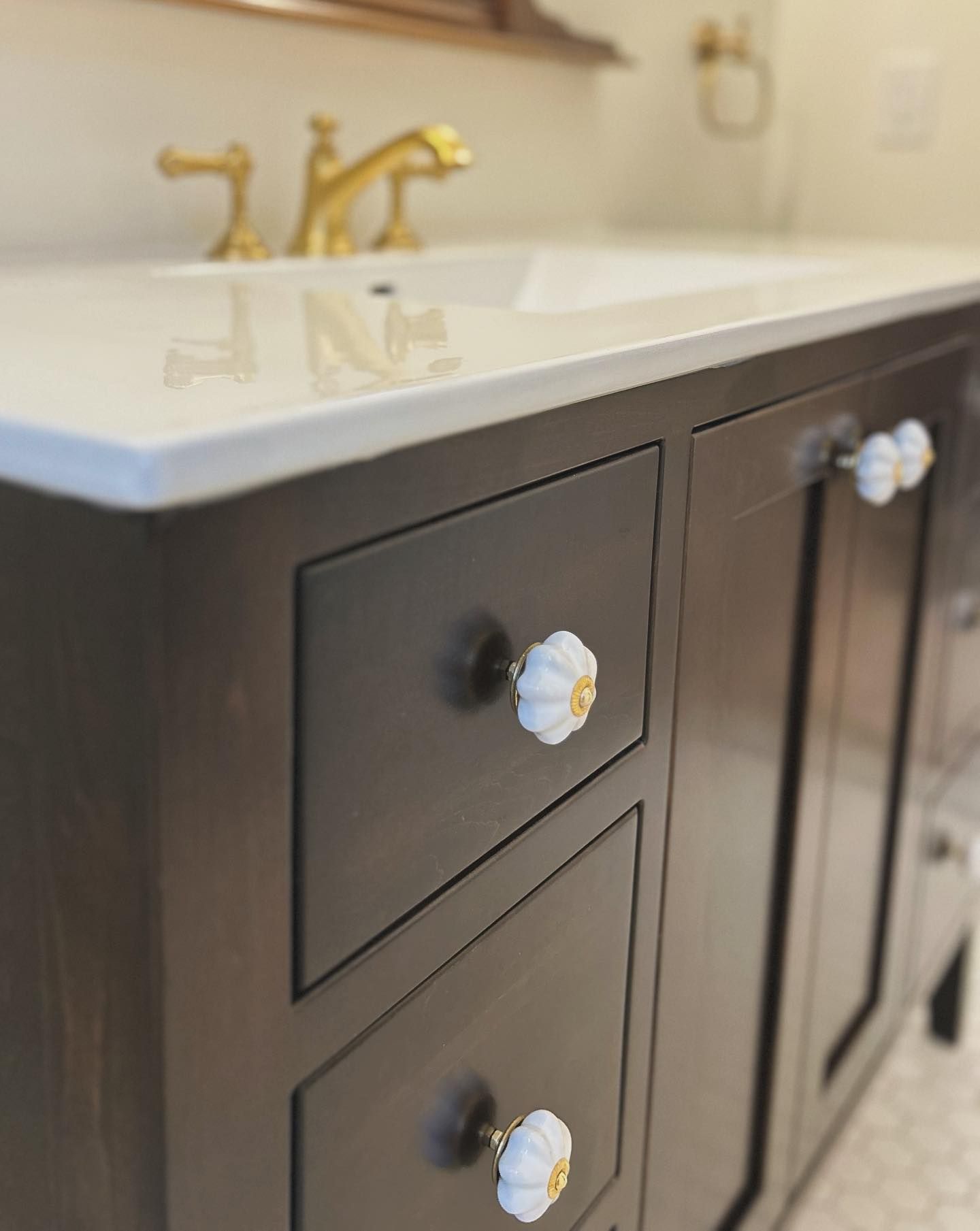Dark brown bathroom vanity with white countertop, gold faucet, and white floral knobs.