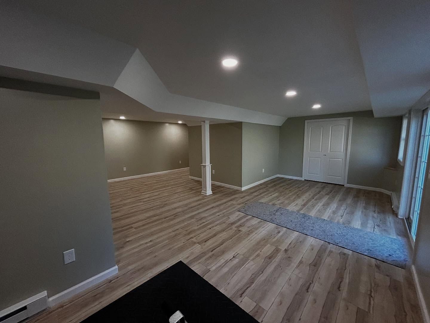 Basement with light wood-look flooring, neutral walls, recessed lighting, and a white door.