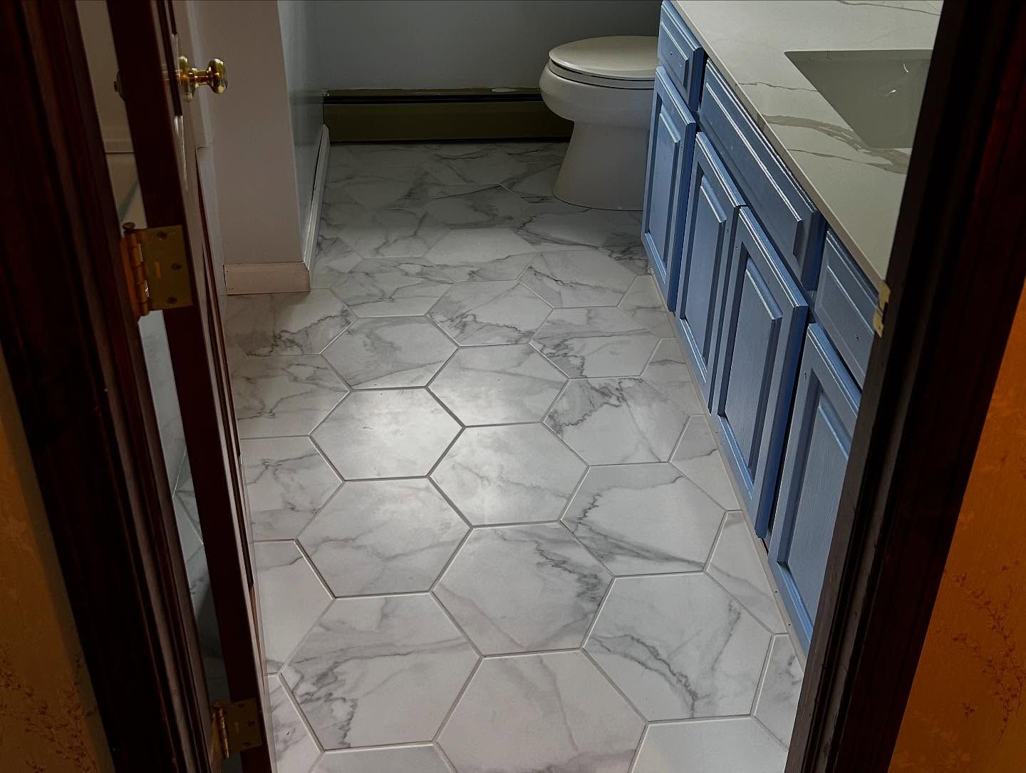Bathroom with hexagon marble tile flooring, blue vanity, and a toilet.