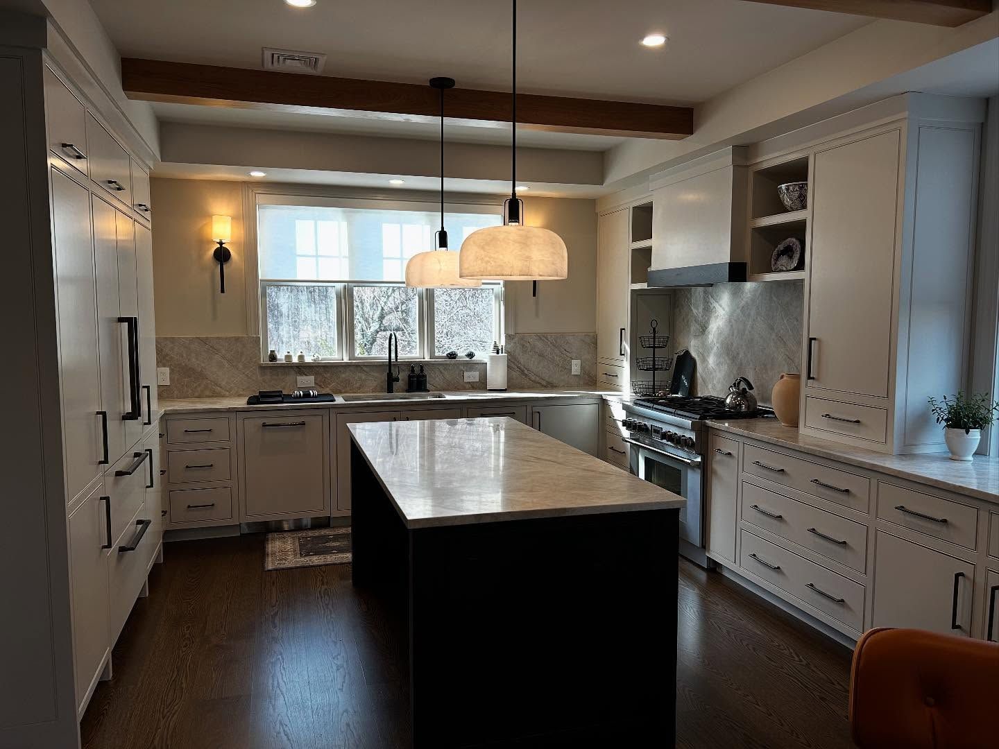 Modern kitchen with dark island, white cabinets, and wood beams.