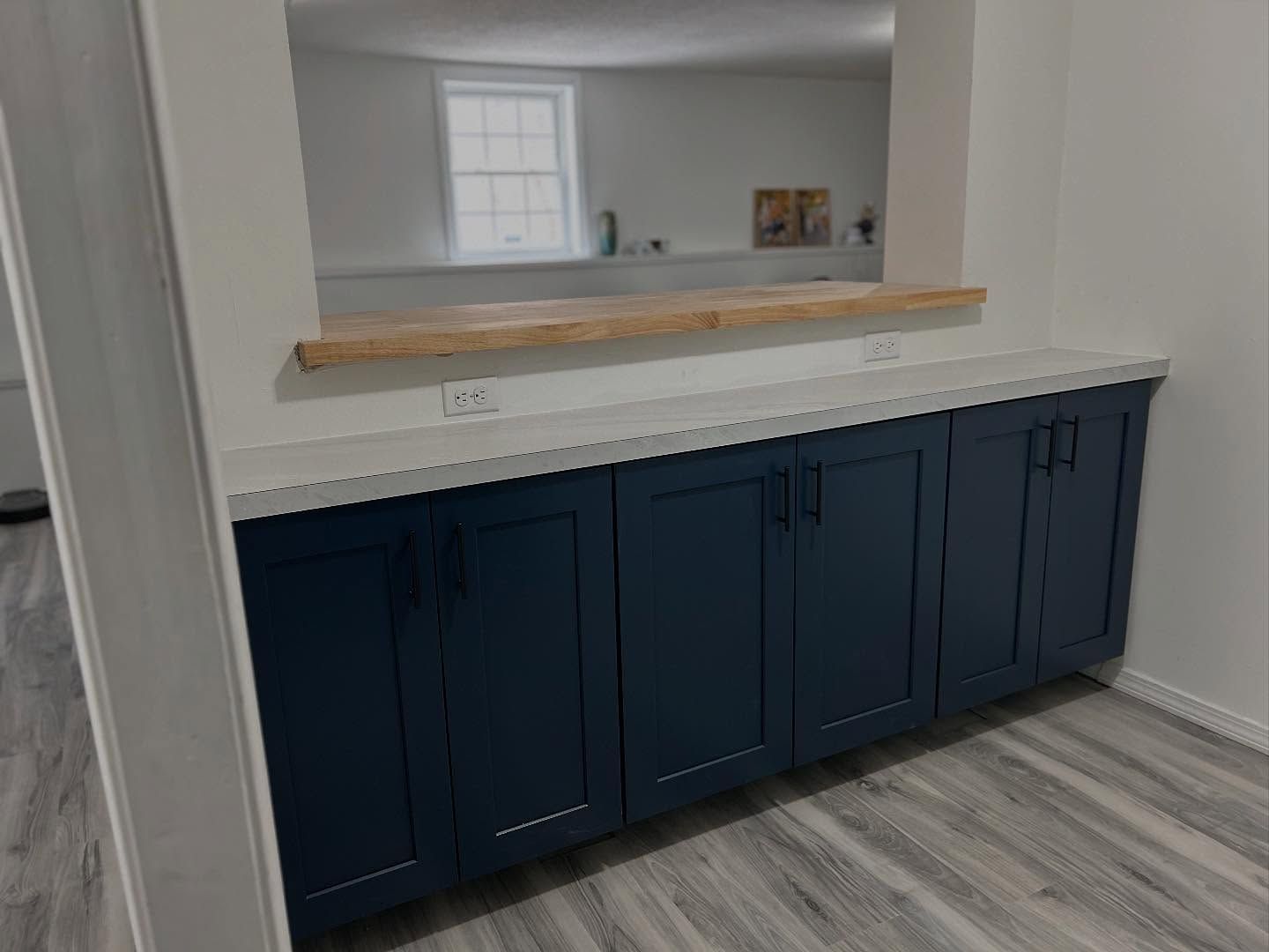 Built-in navy cabinets with a white countertop under a pass-through window with a wood ledge.