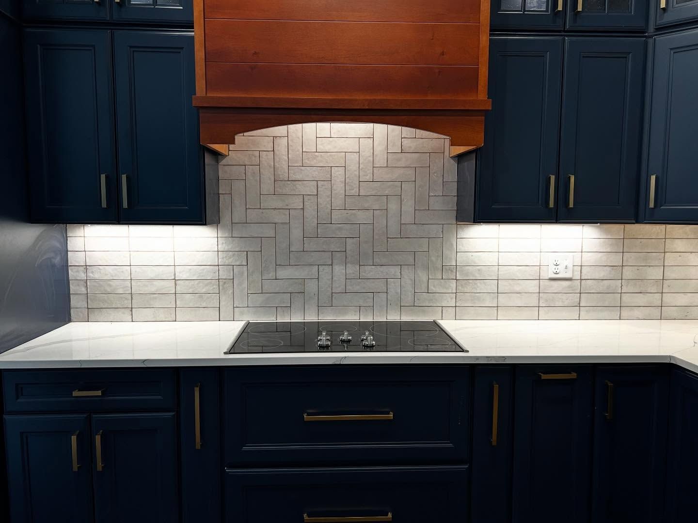 Navy blue kitchen with wood range hood, gray backsplash, and gold hardware.