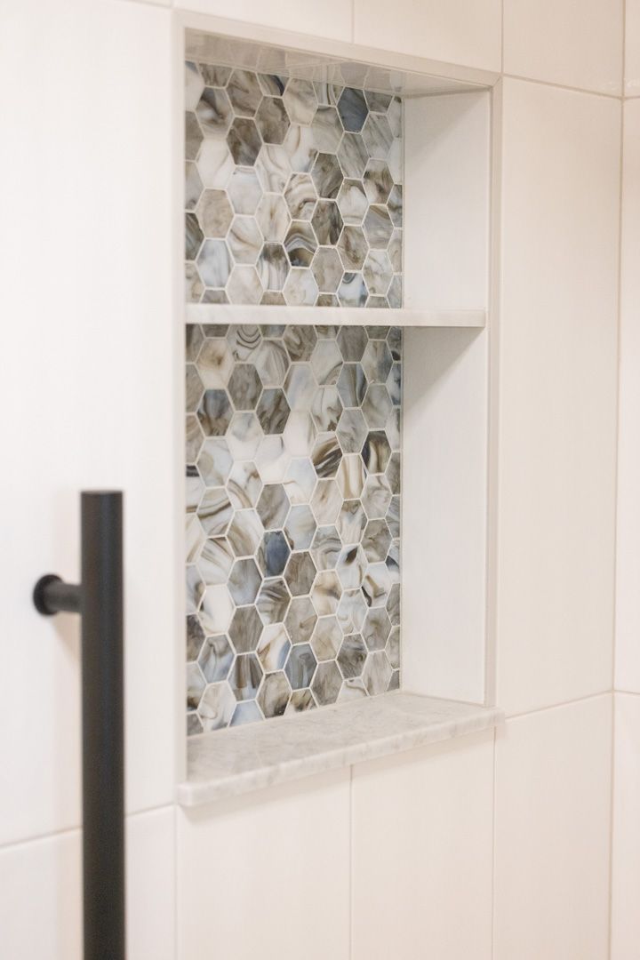 Shower niche with gray, blue, and white mosaic tile. White shelves. Black towel bar.