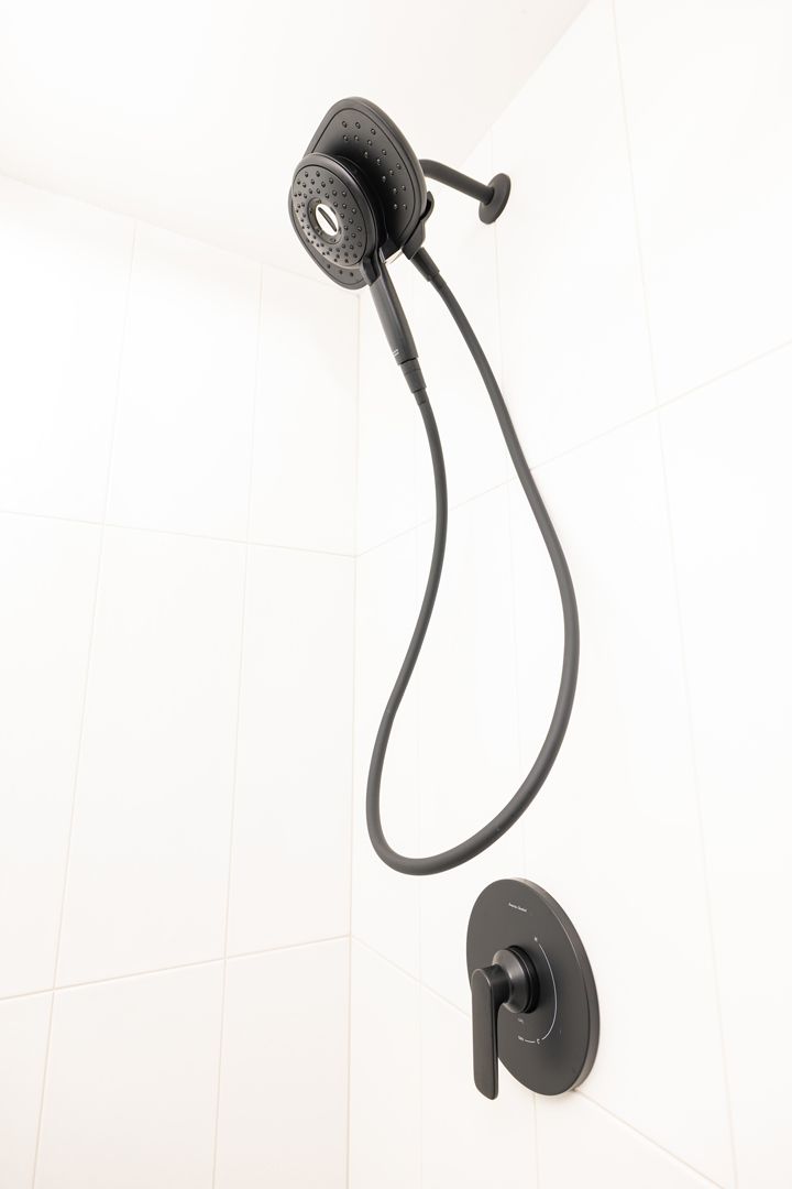Black shower head and faucet on white tiled wall.