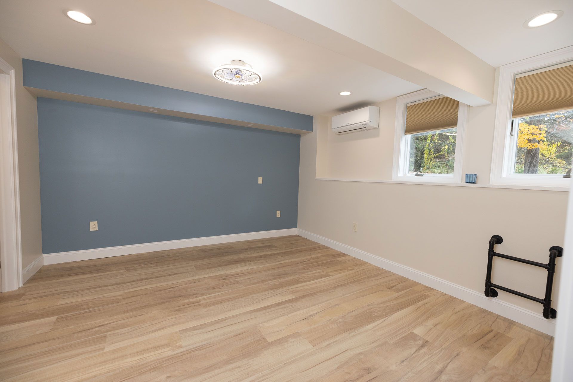 Empty room with wood floors, blue accent wall, windows with shades, and a ceiling light.