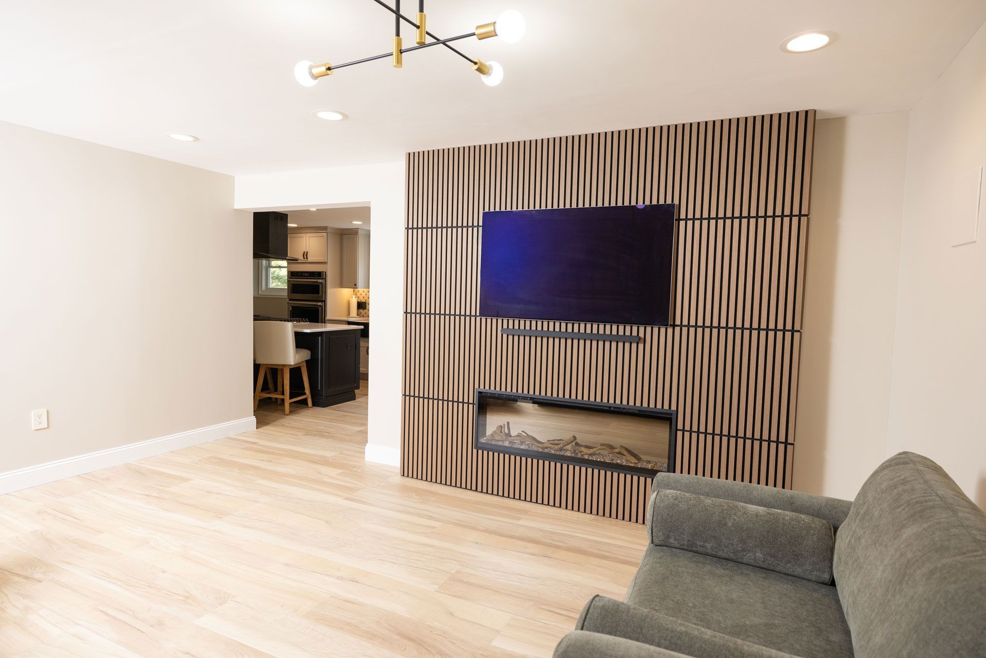 Living room with wood panel accent wall, fireplace, and TV. Kitchen visible in the background.
