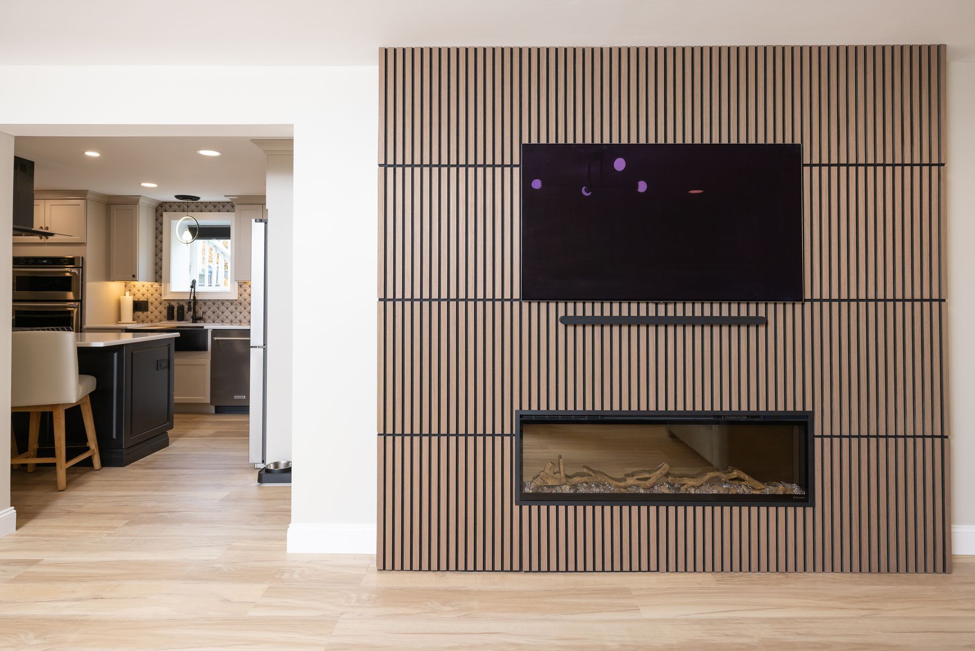 Living room with wood panel wall, TV, and fireplace. Kitchen visible in the background.