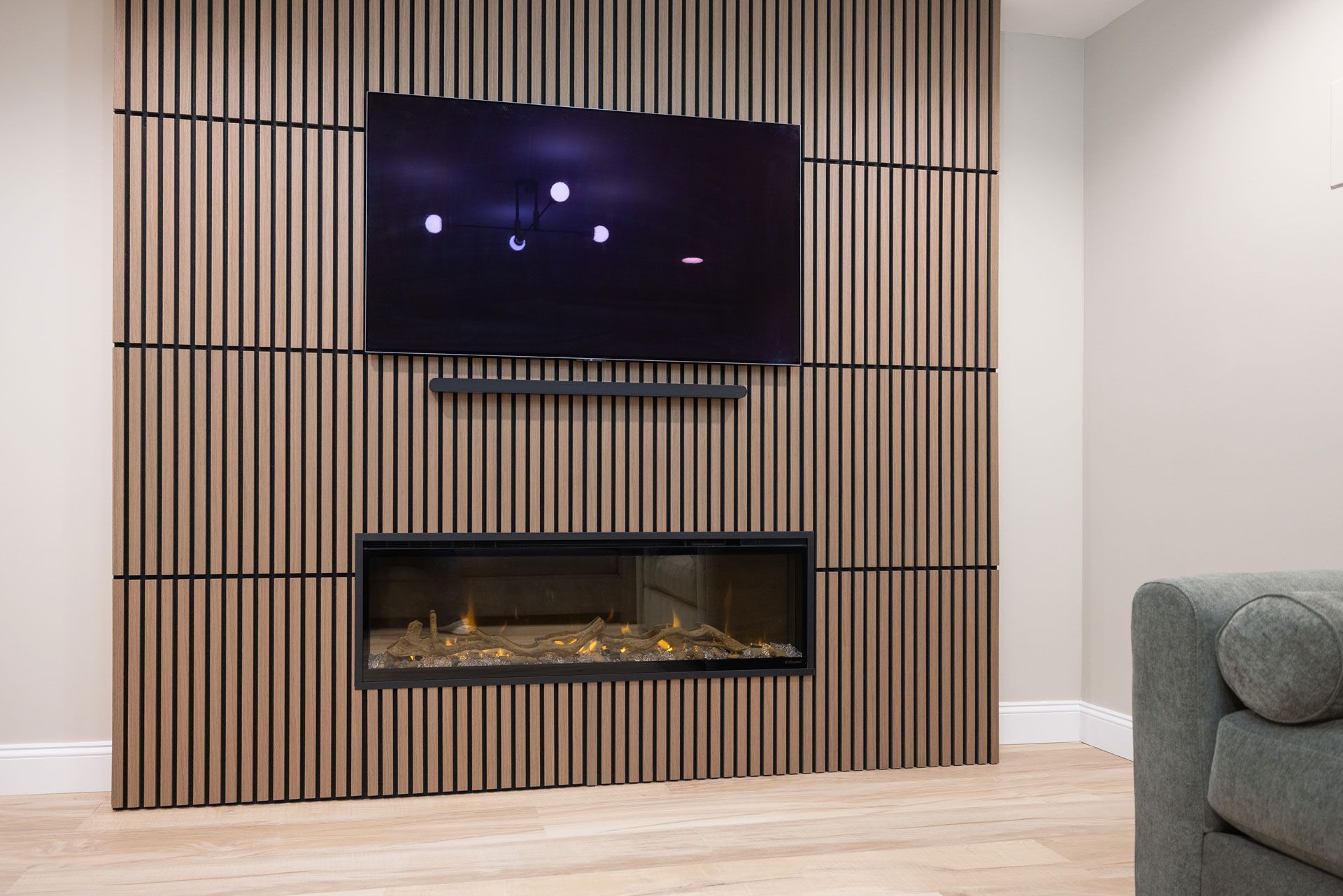 Wooden slat wall with mounted TV, soundbar, and fireplace. Light wood tones, modern design.