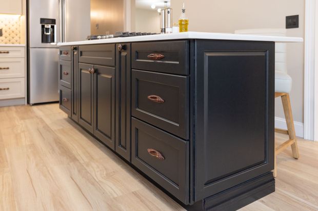 Person in blue jacket using a pencil and ruler to draw on blueprints at a wooden table, next to a stack of wooden boards.
