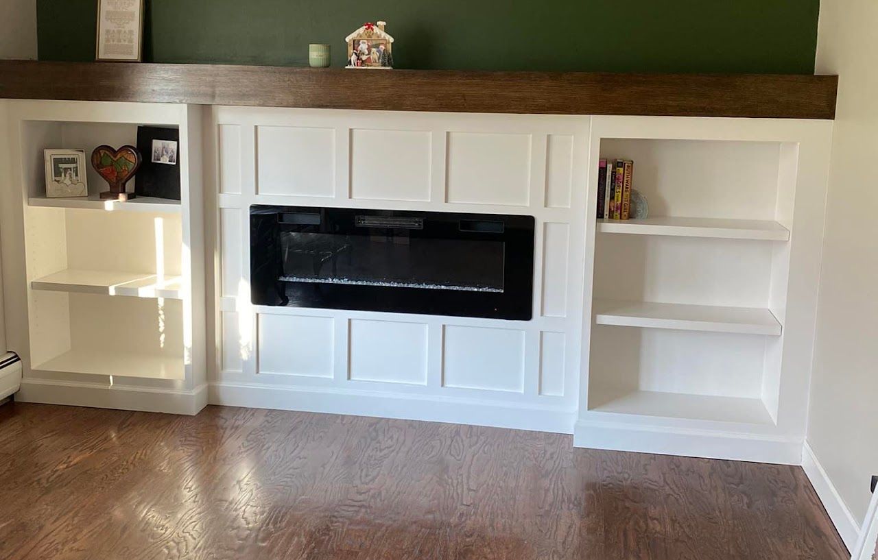 White built-in fireplace with shelves, dark mantel, black fireplace insert, on wood floor, against a green wall.