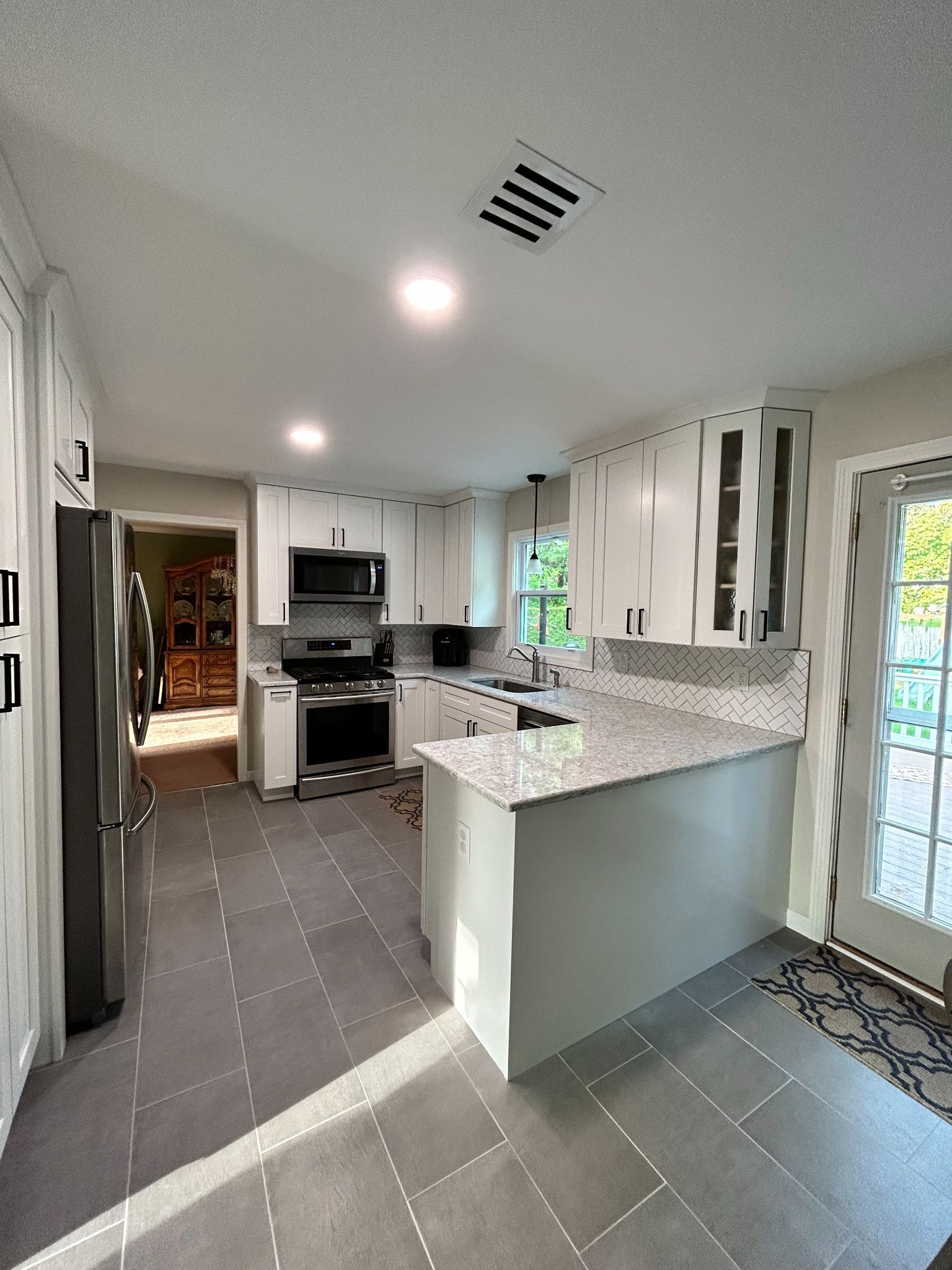 White kitchen with gray tile floor, stainless steel appliances, and a granite countertop.