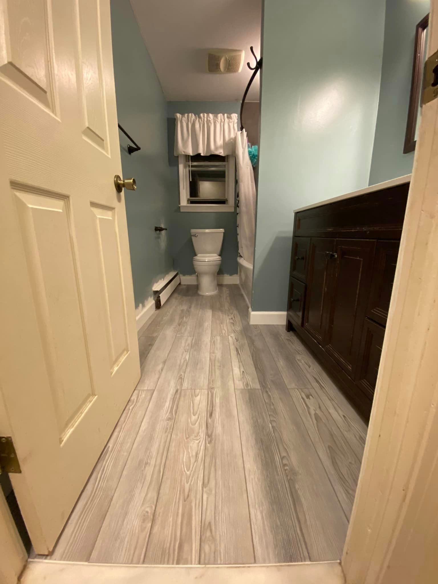 Bathroom interior, light wood-look floor, blue walls, toilet, dark wooden vanity, open door.