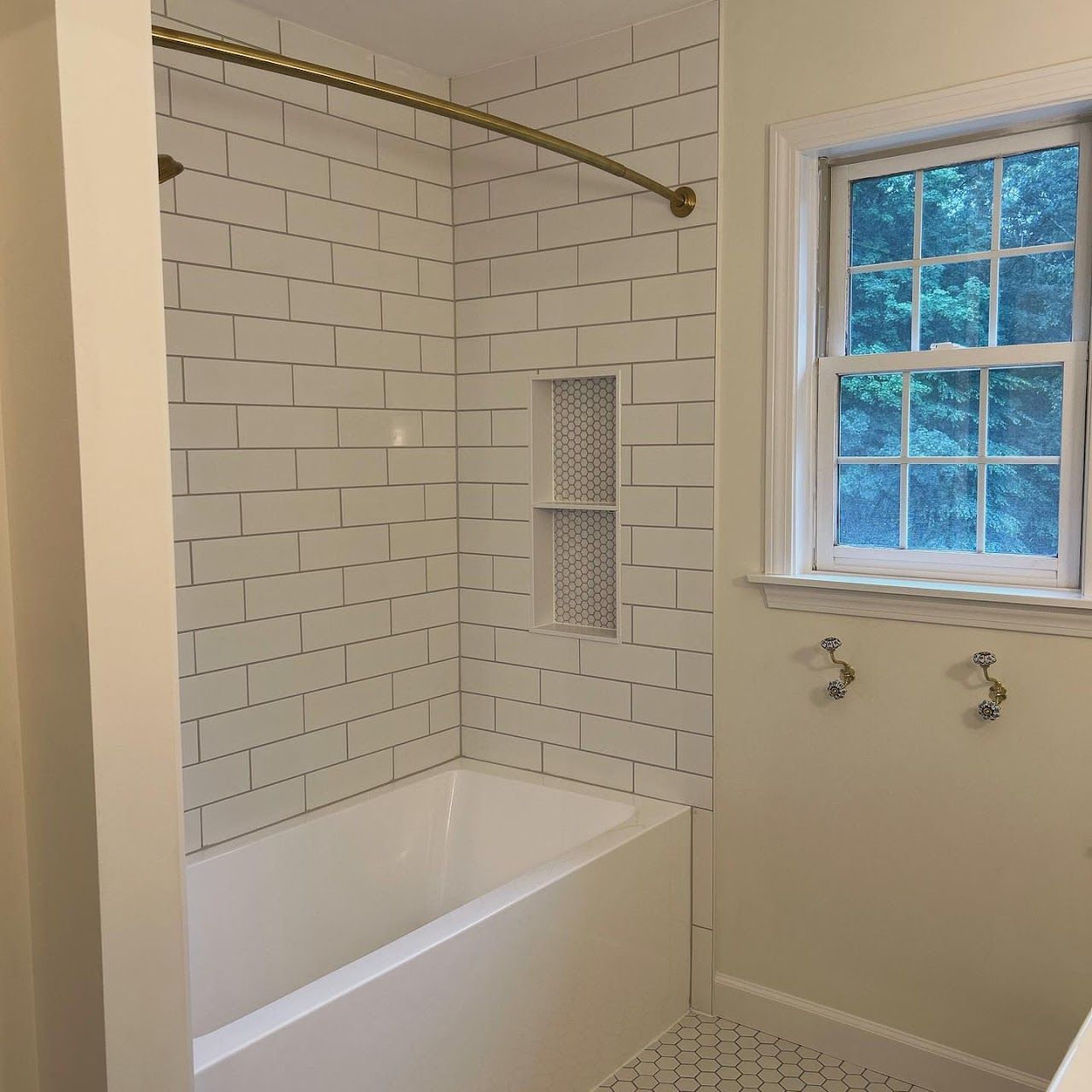 Bathroom with white subway tile shower, gold shower rod, and small window.