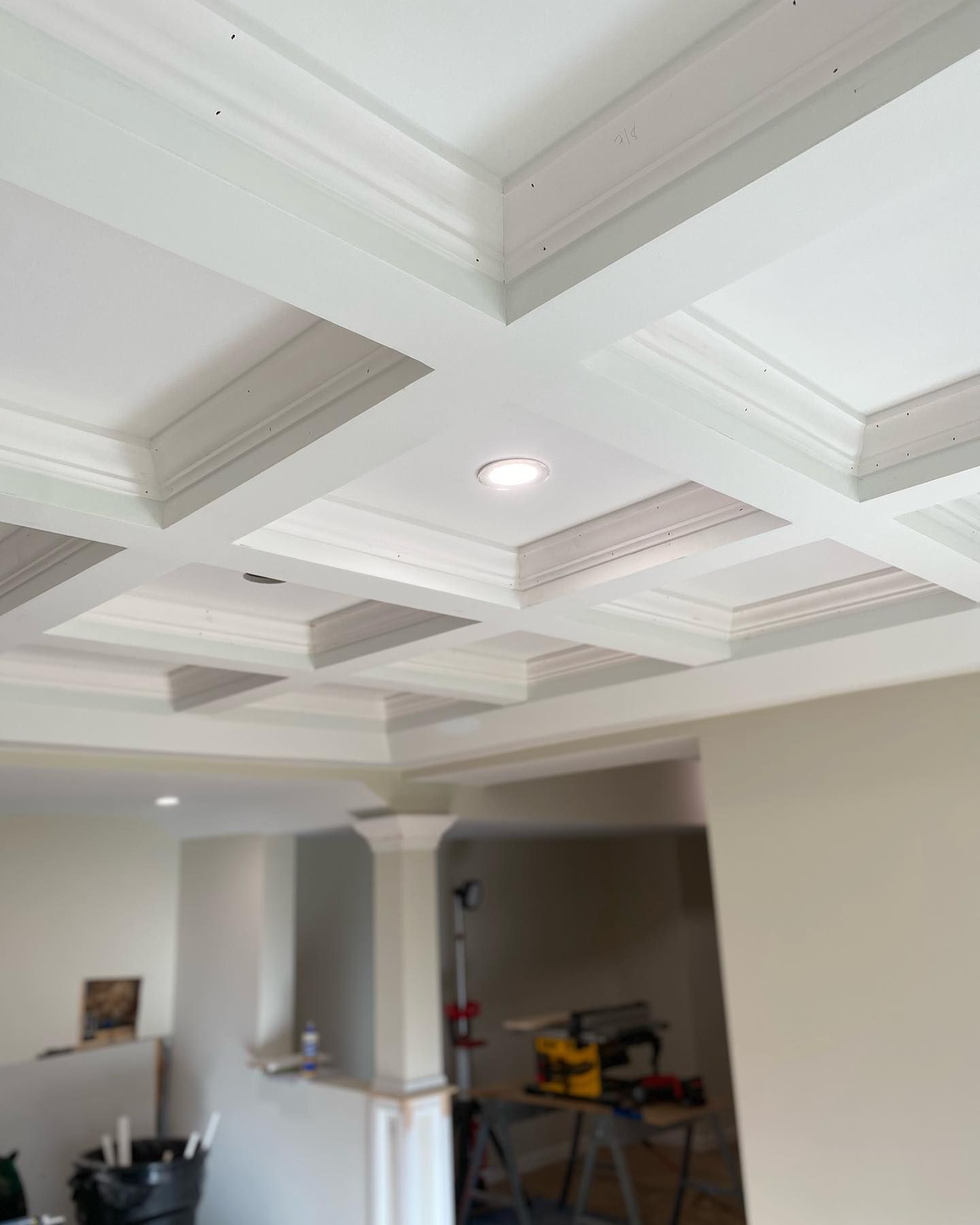 White coffered ceiling with recessed lighting; room under construction with a pillar.