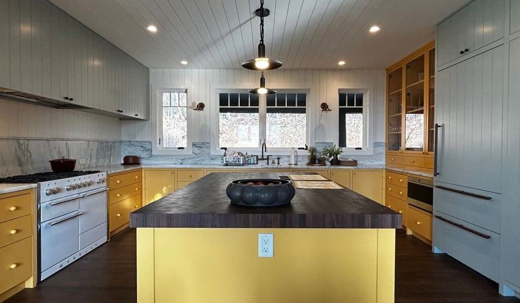 Modern kitchen with yellow cabinetry, marble counters, and a dark wood island.