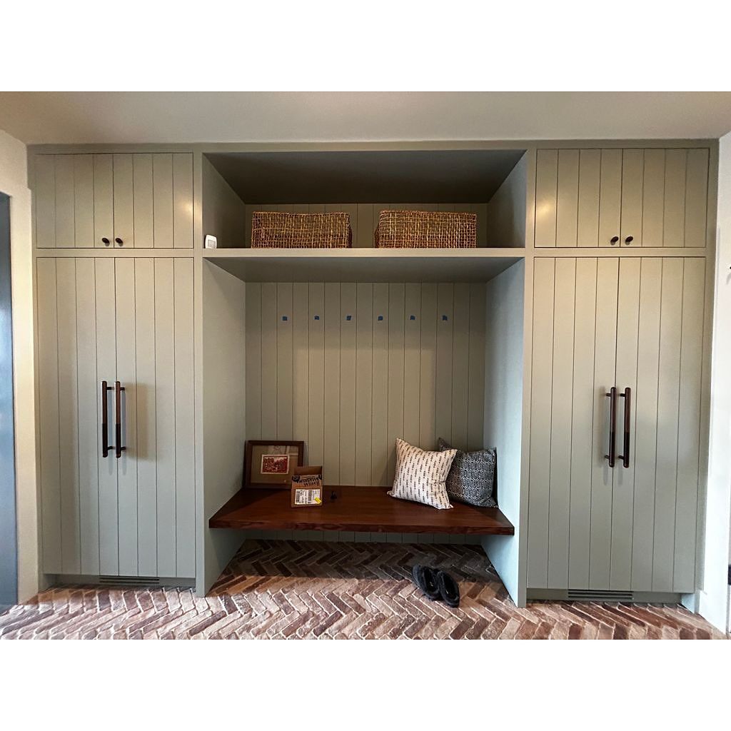 Built-in storage unit with cabinets and bench. Light green painted wood. Baskets, bench with pillows.