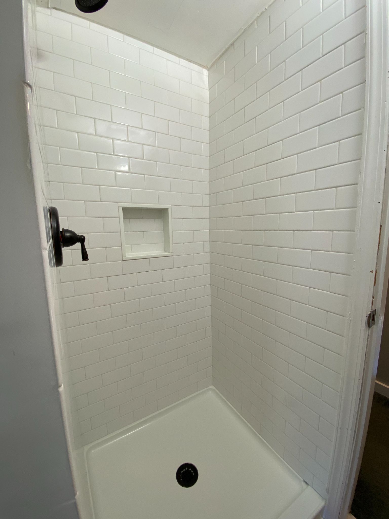 White-tiled shower with black fixtures and a recessed shelf.