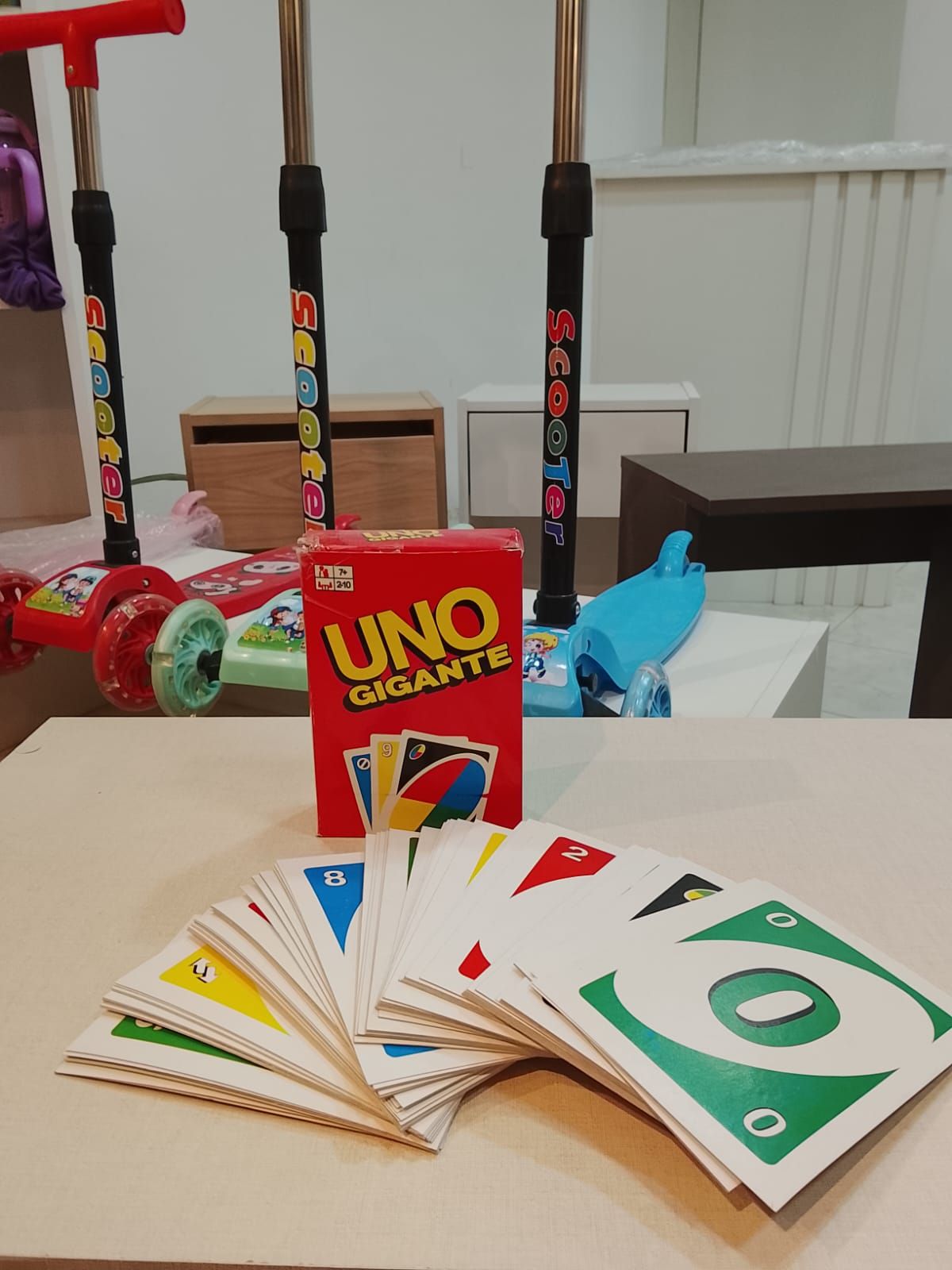 Juego de cartas Uno Gigante con una mano de cartas en primer plano y patinetes al fondo.