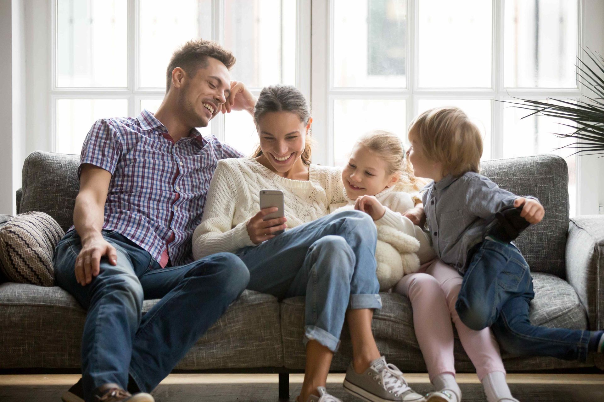 a family sits on a couch looking at a cell phone