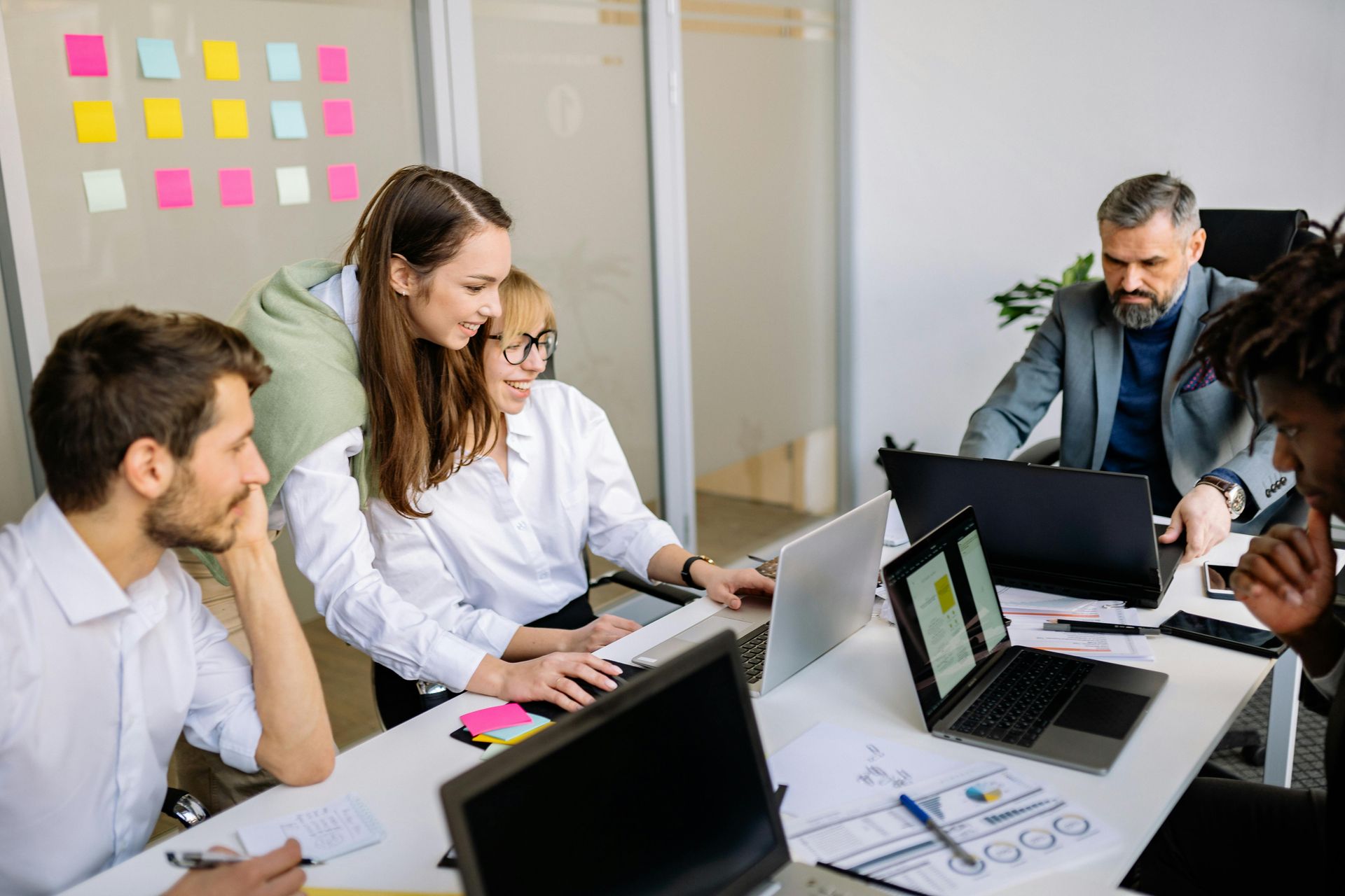 Group of people collaborating around a table in an office setting, using laptops and discussing ideas.