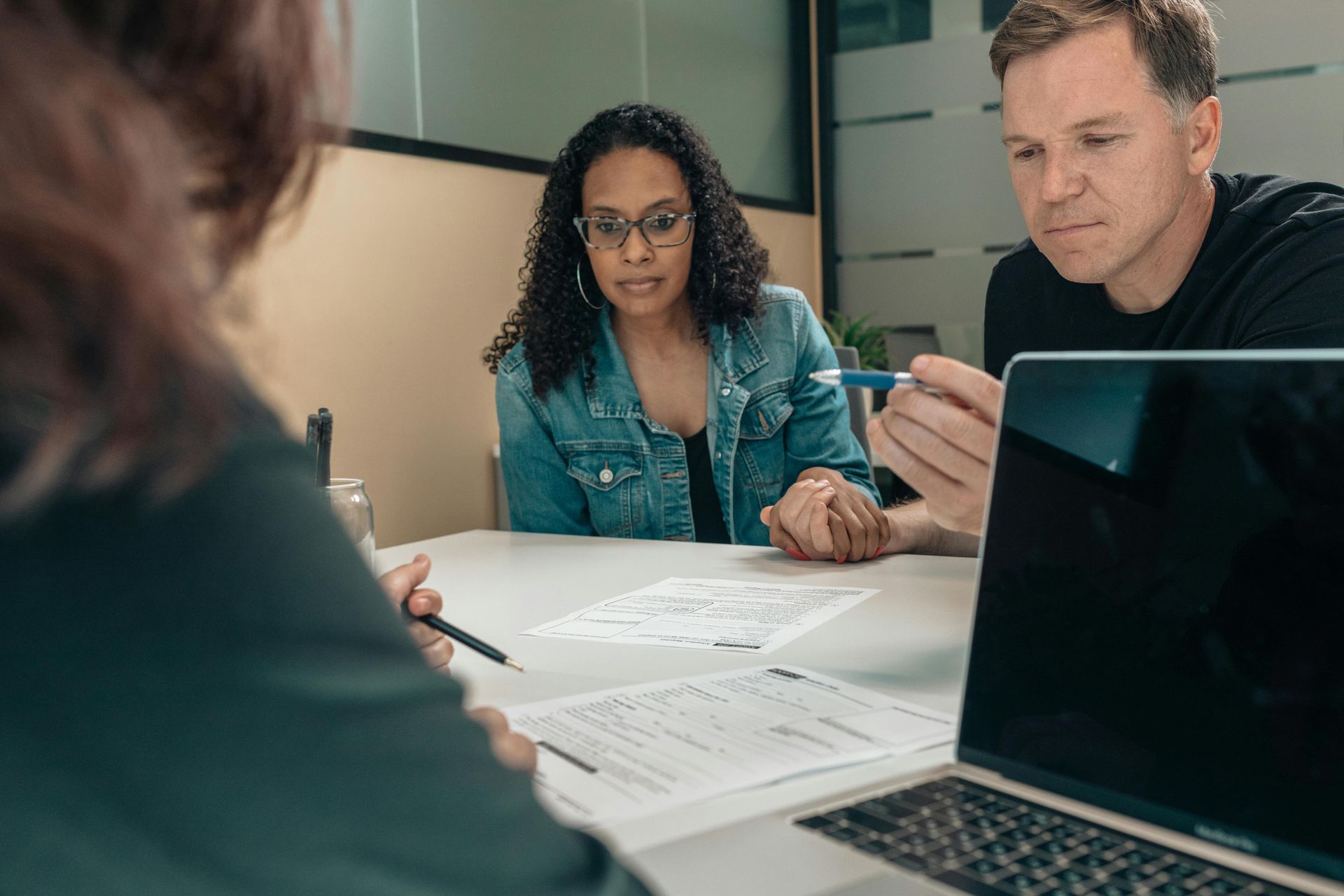 A couple reviews paperwork with a professional at a table; all are focused, the man is pointing at a document.