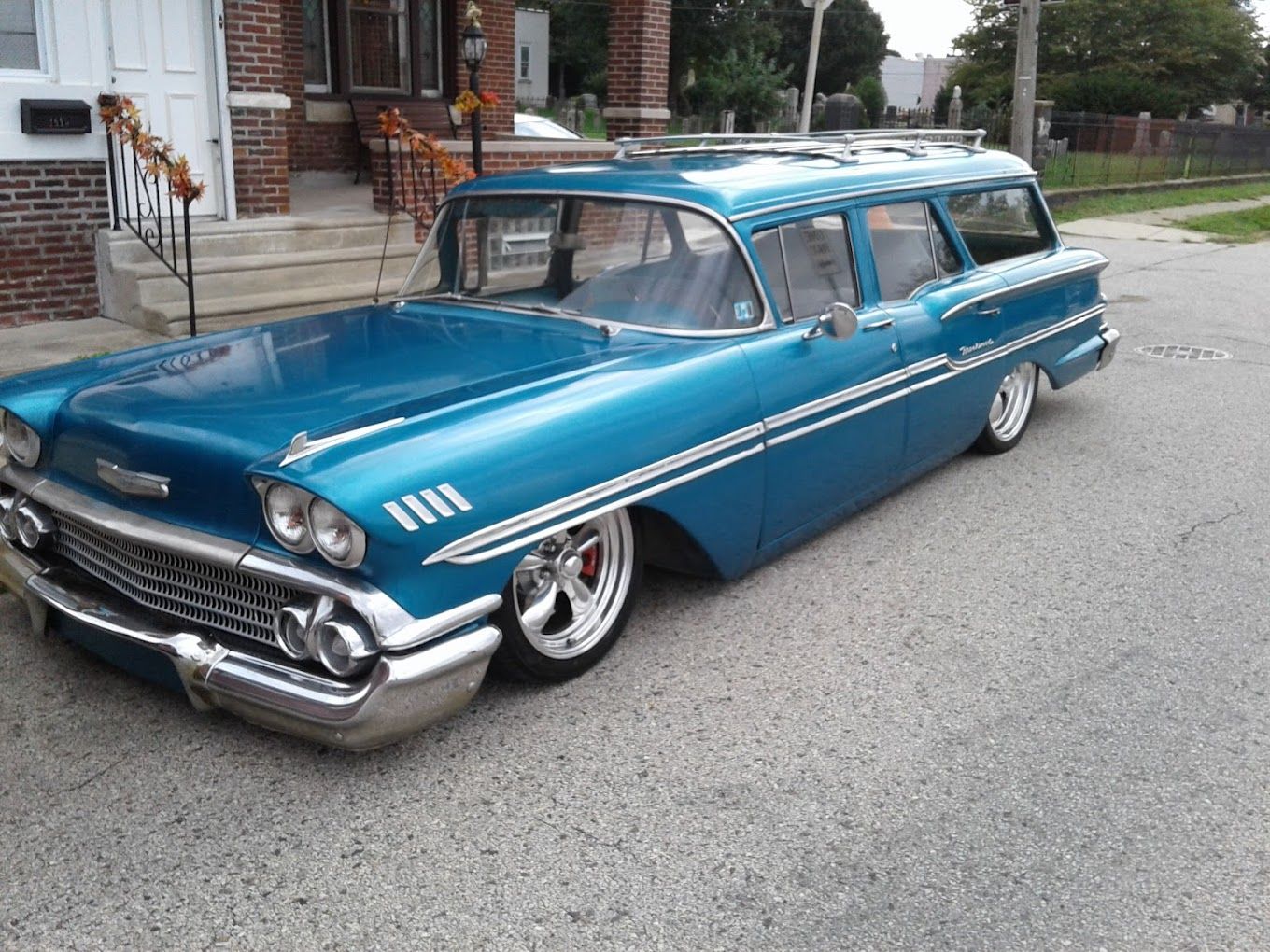 A blue car is parked in front of a brick house.