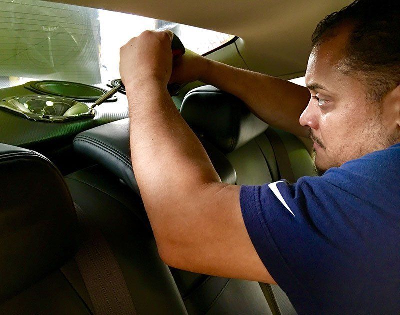A man in a blue shirt is working on the back seat of a car