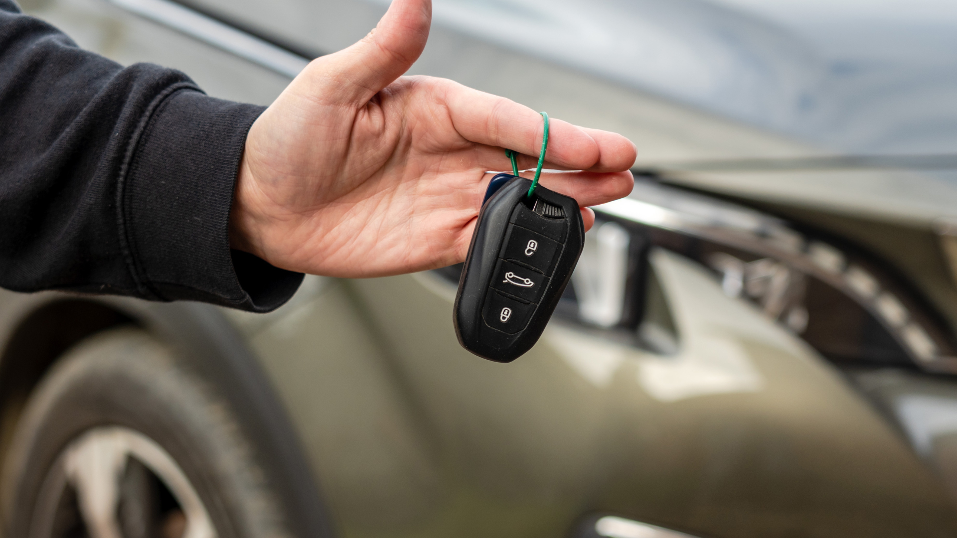 A person is holding a car key in front of a car.