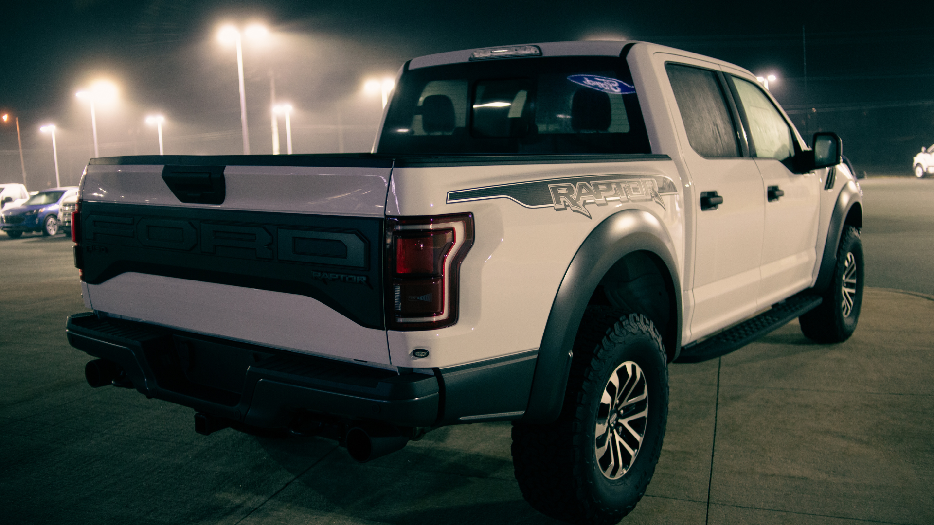 A white pickup truck is parked in a parking lot at night.