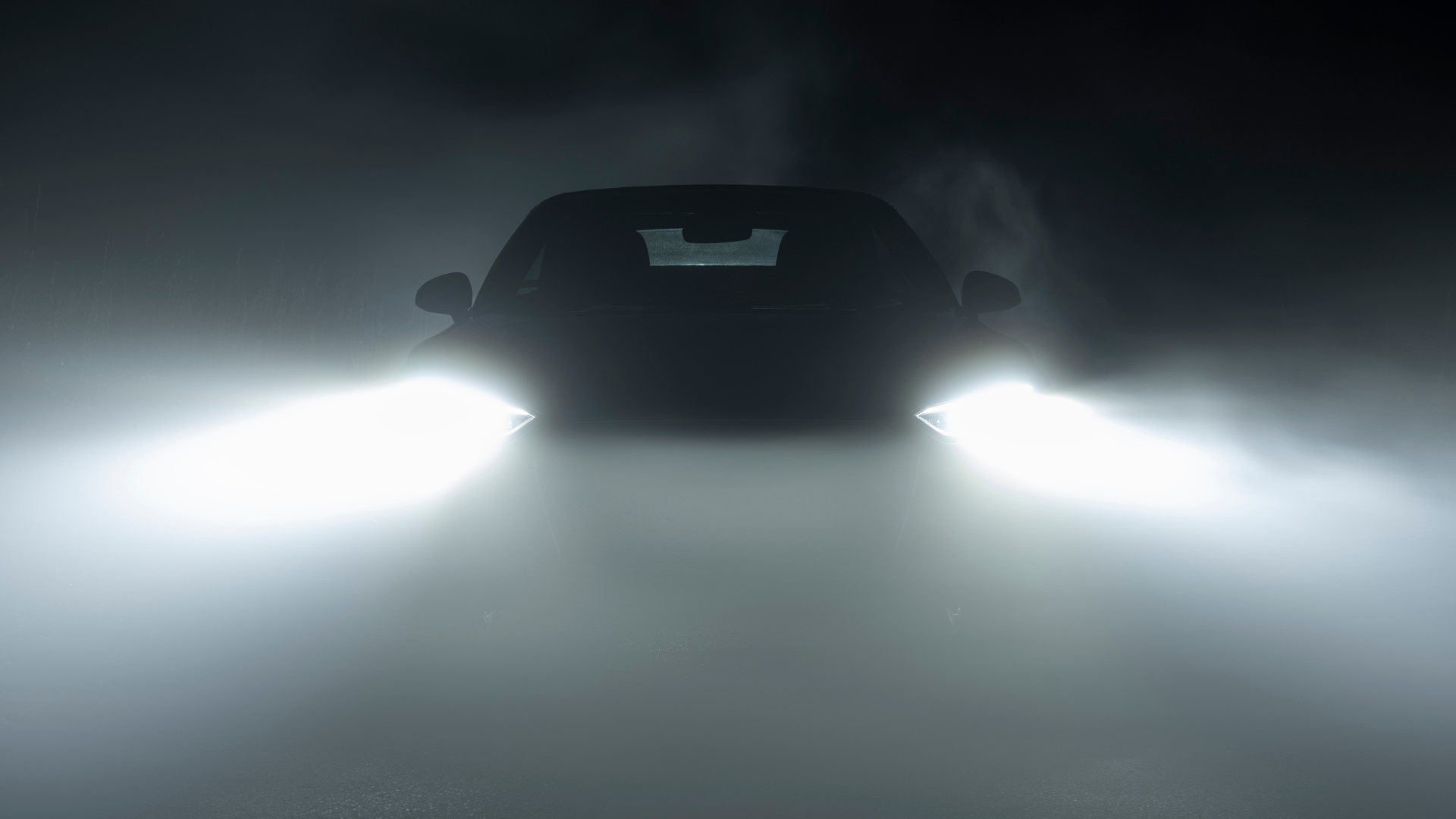 A car is driving through a foggy night with its headlights on.