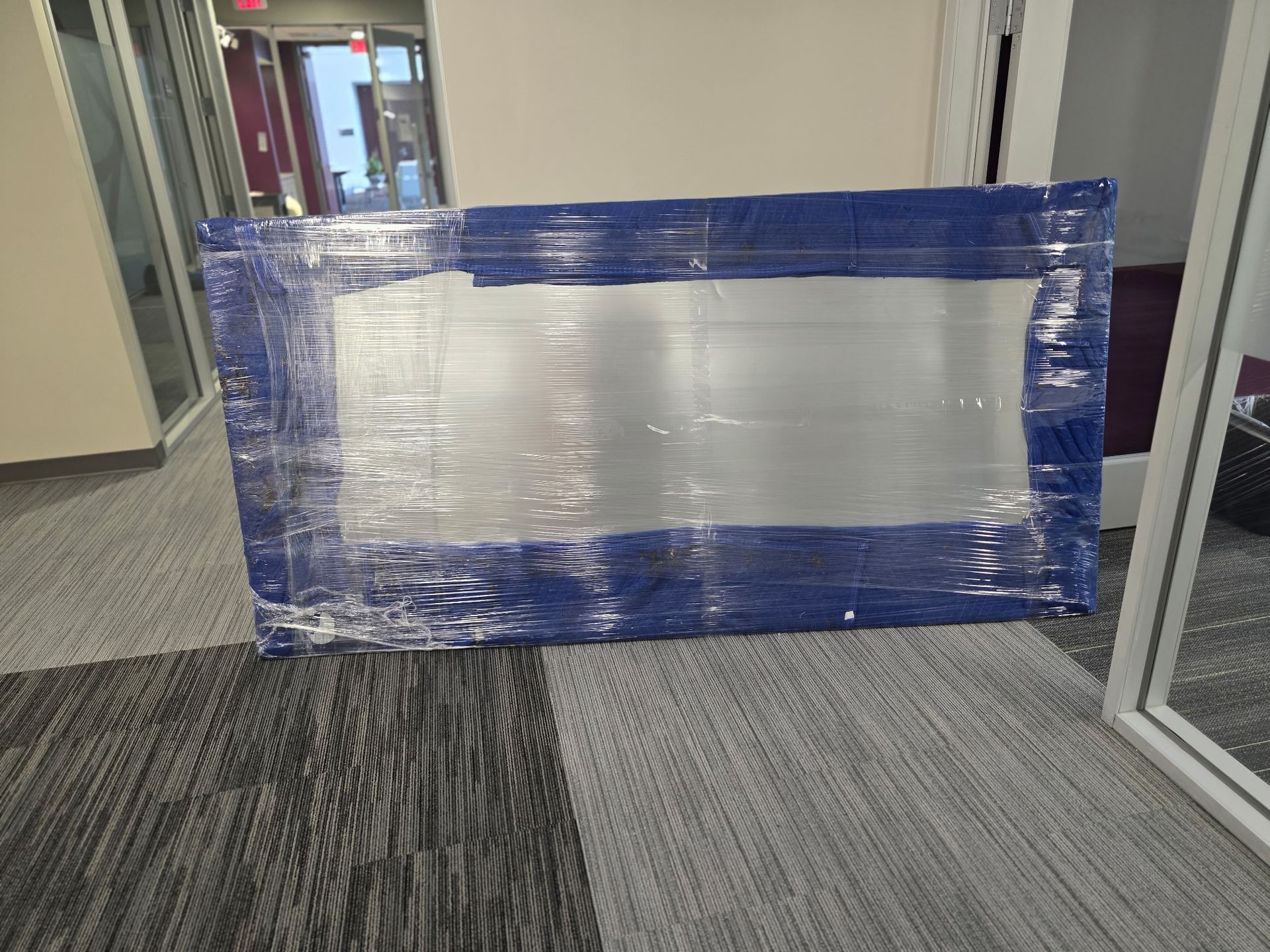 A rectangular object wrapped in blue tape and clear plastic, lying on a patterned gray floor.